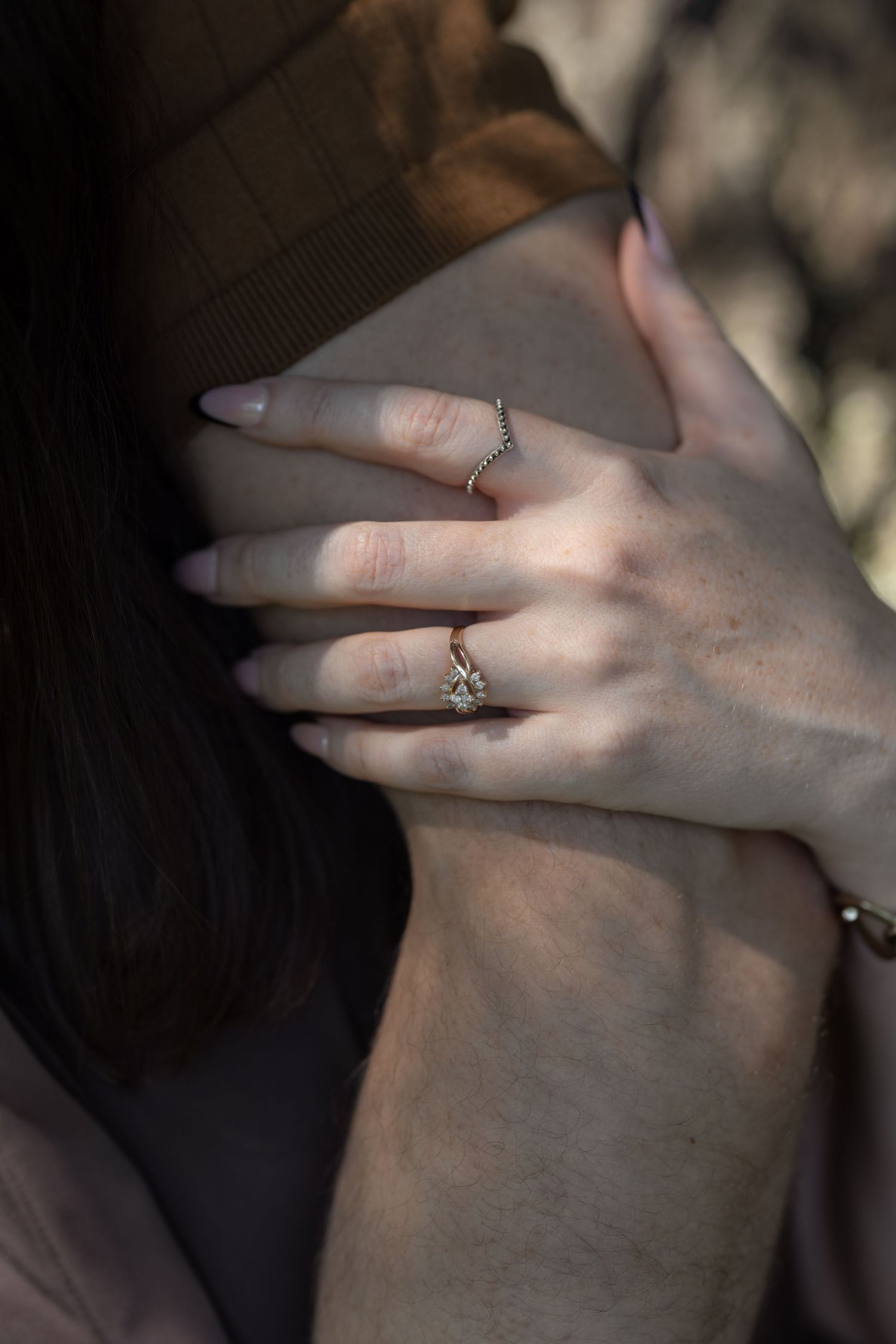 Close-up of a woman's hand wearing a delicate diamond engagement ring and bracelet, resting on someone's arm.