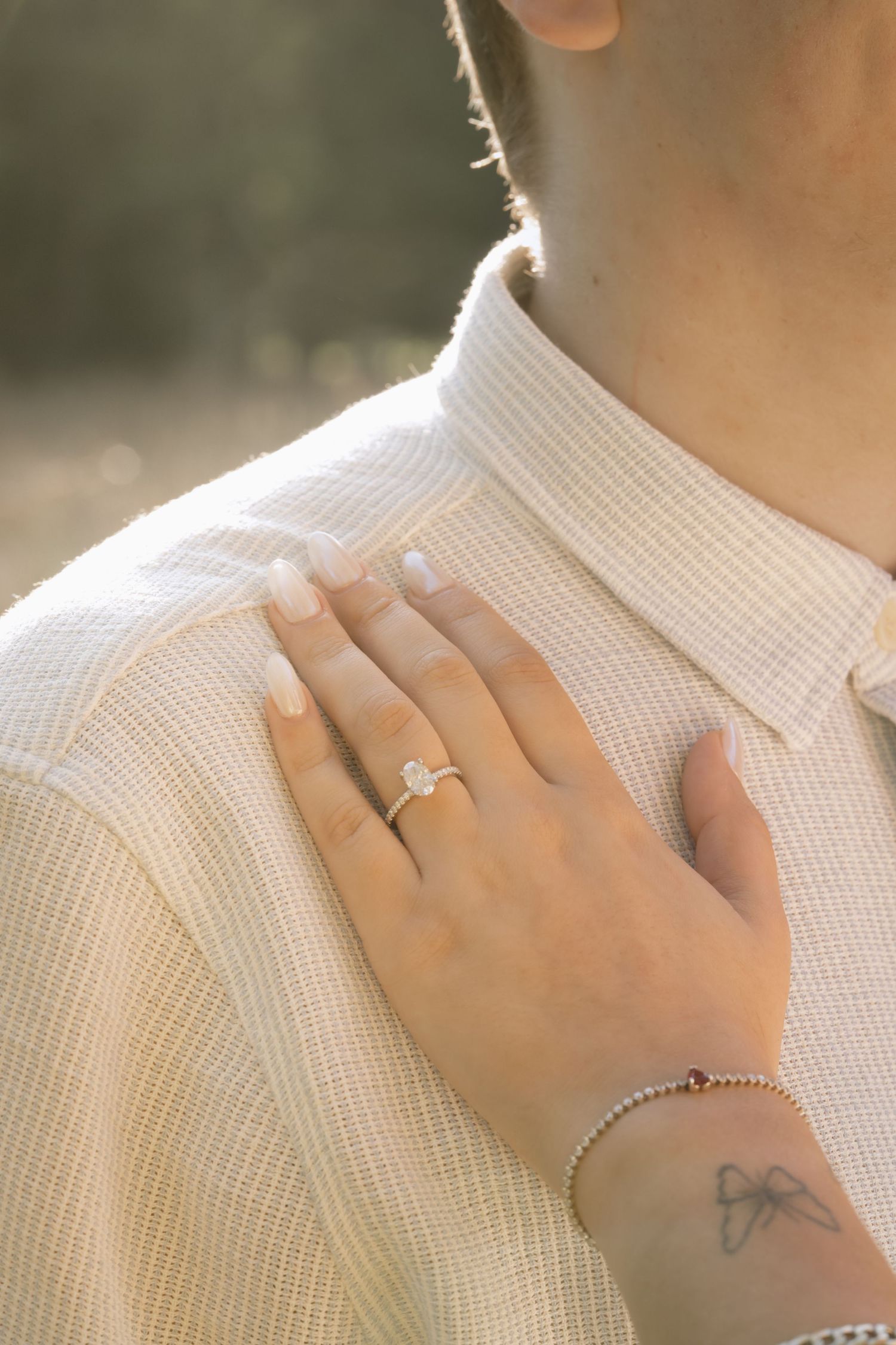 Close-up of a hand wearing an engagement ring resting on a white knit sweater with a small tattoo visible.  Rochester NY film engagement pho
