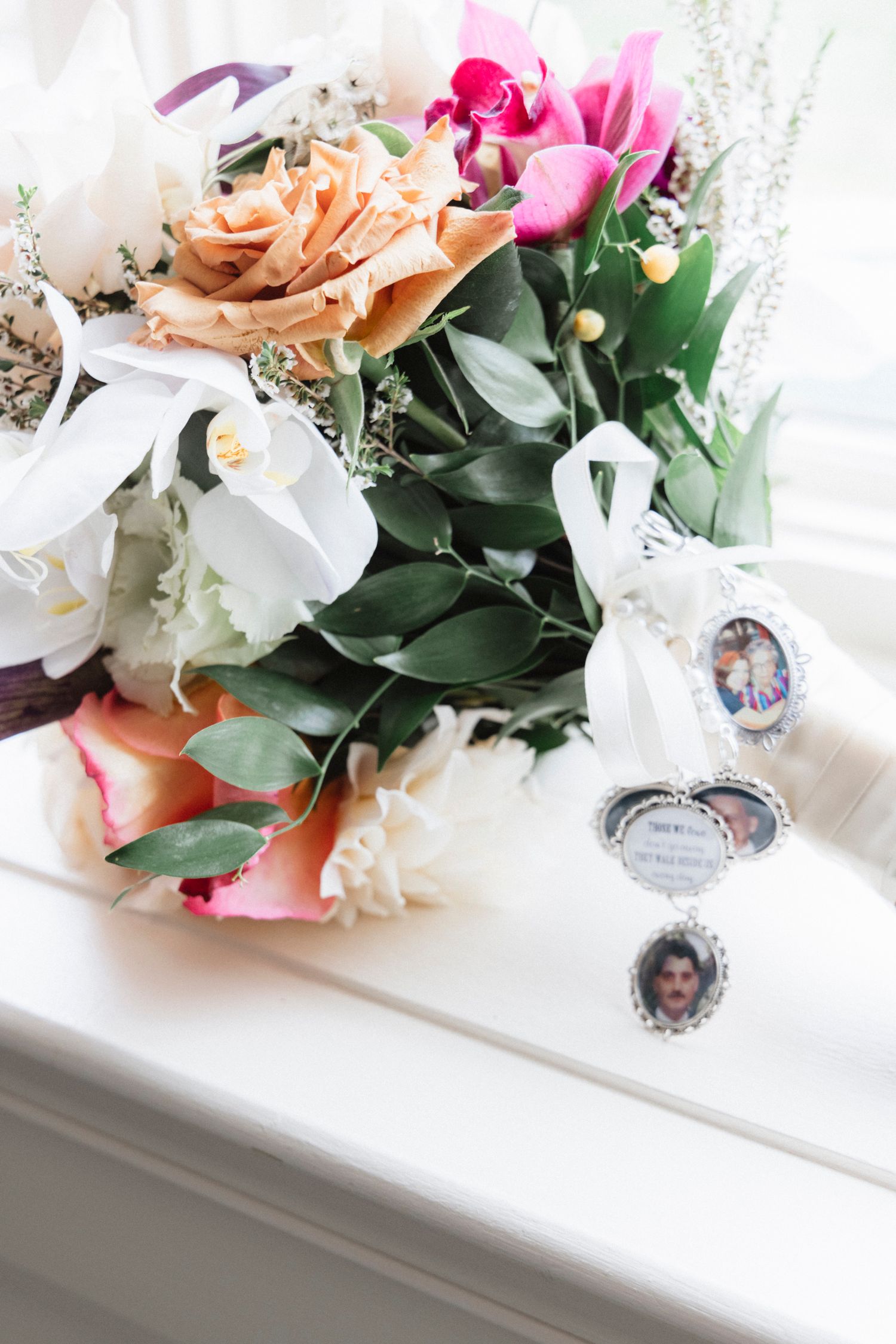 Colorful wedding bouquet with pink and peach roses arranged on a white surface with decorative details.Rochester NY documentary wedding phot