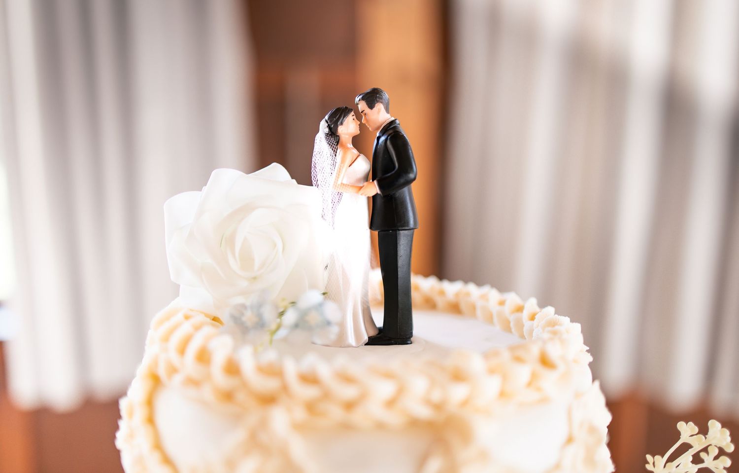 Cake topper of a bride and groom with a white rose on a 3 tier wedding cake