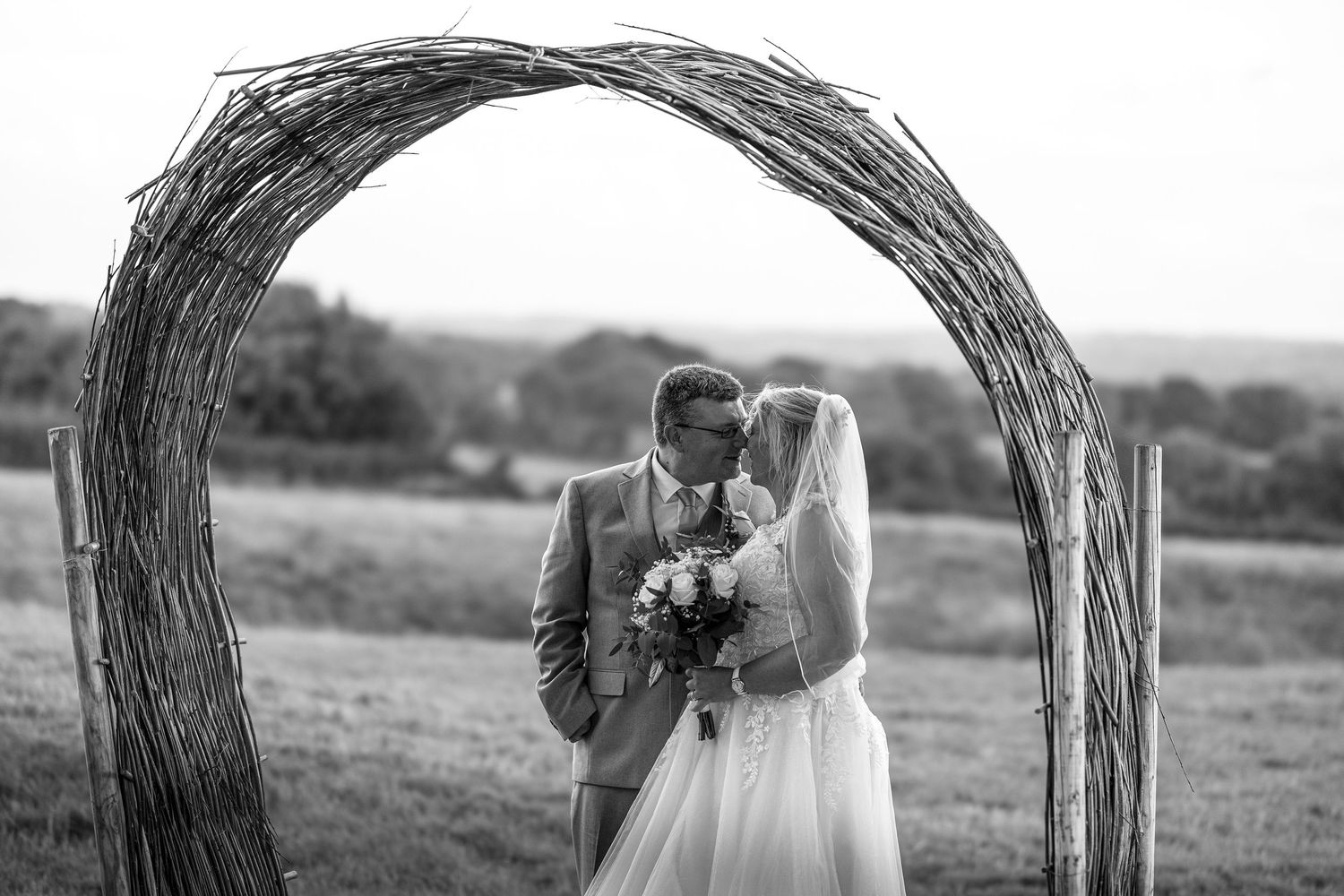 Black and White image of bride and groom under a wicker style archway