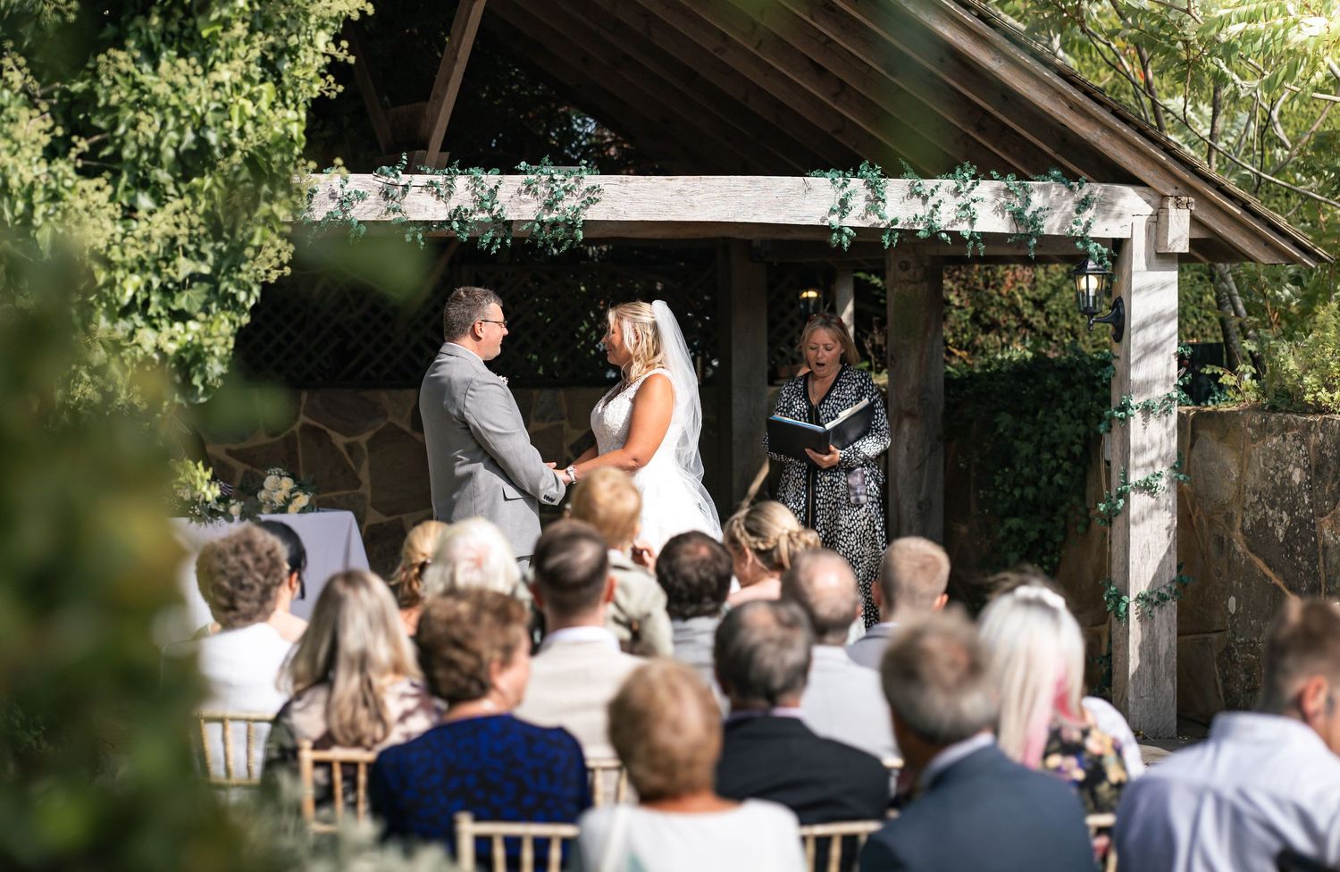 Ceremony moment of Bride and Groom holding hands from the back  including guests