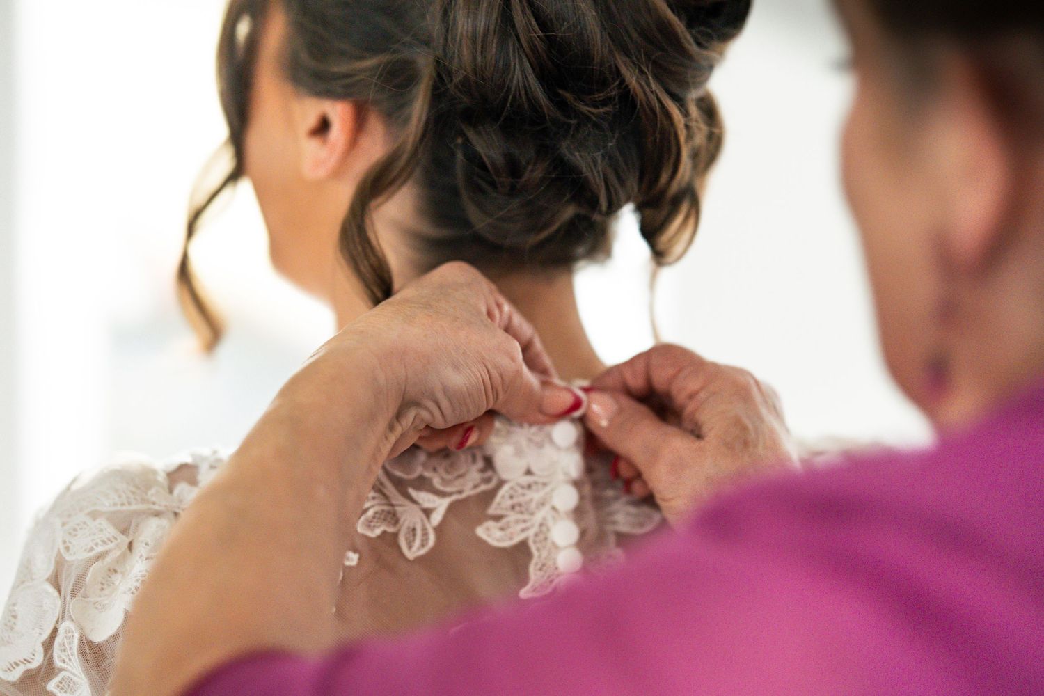 Candid moment of mother of bride securing buttons on wedding dress