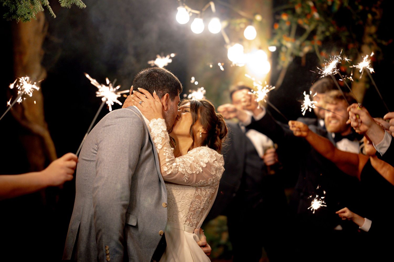 Bride and Groom sharing a kiss with guests holding sparklers