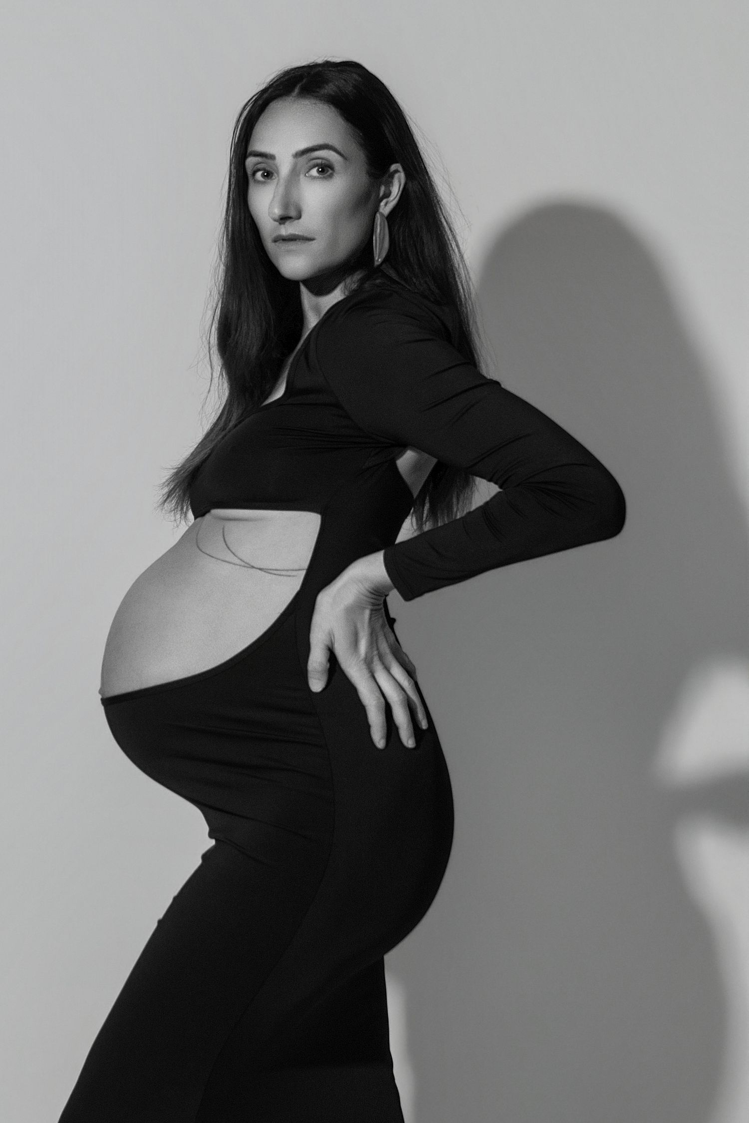 Black and white photo of a pregnant woman in a black cutout dress posing confidently against a light background.