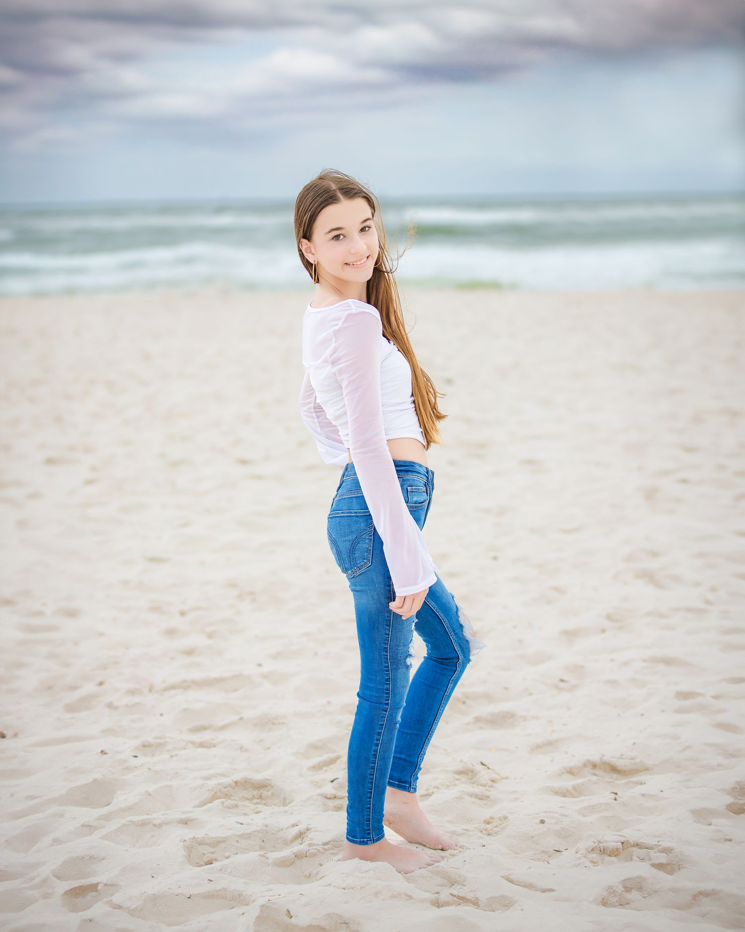 A casual beach portrait with soft pastel colors and ocean waves in the background.