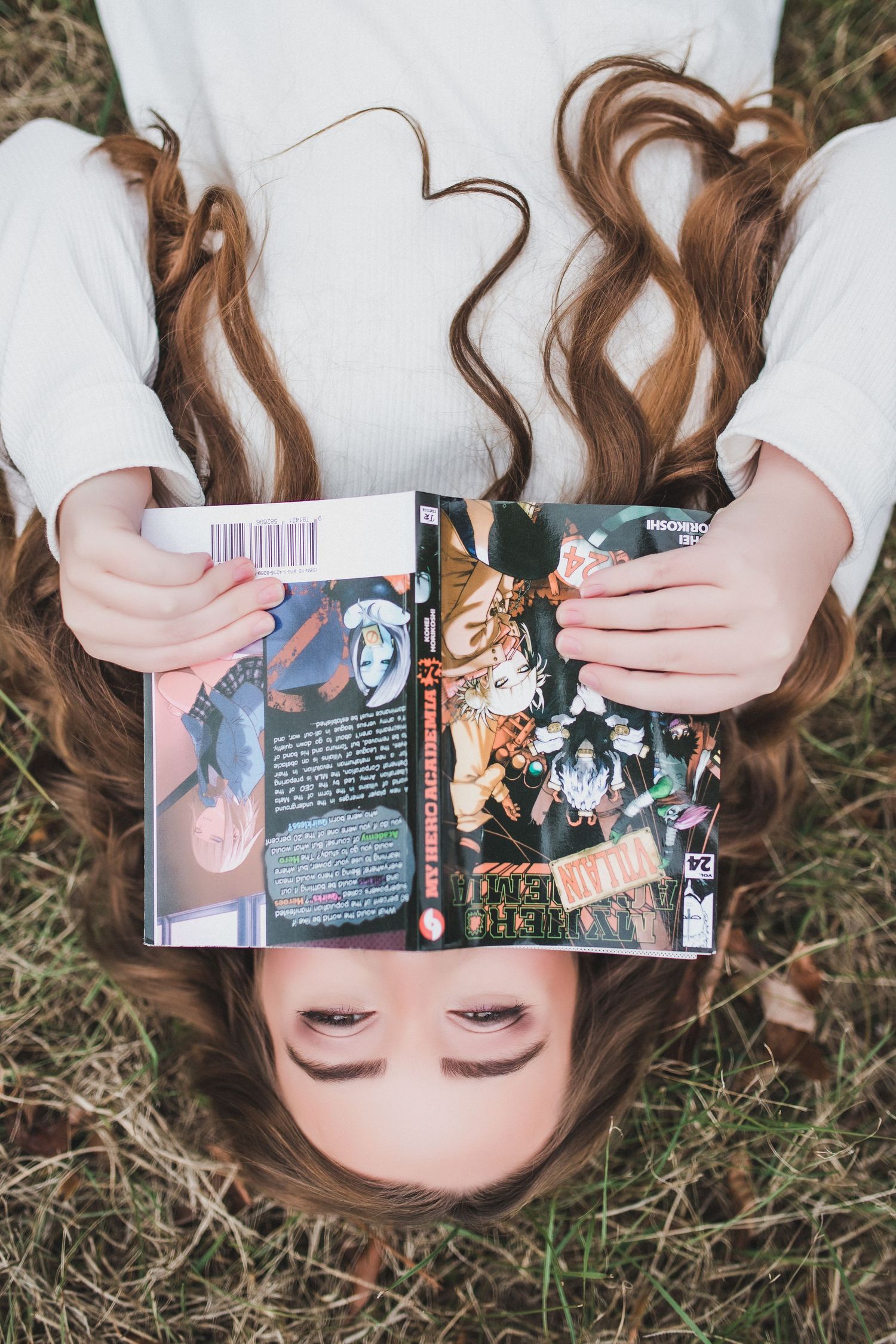 Creative overhead shot of someone lying on grass holding an open manga book.