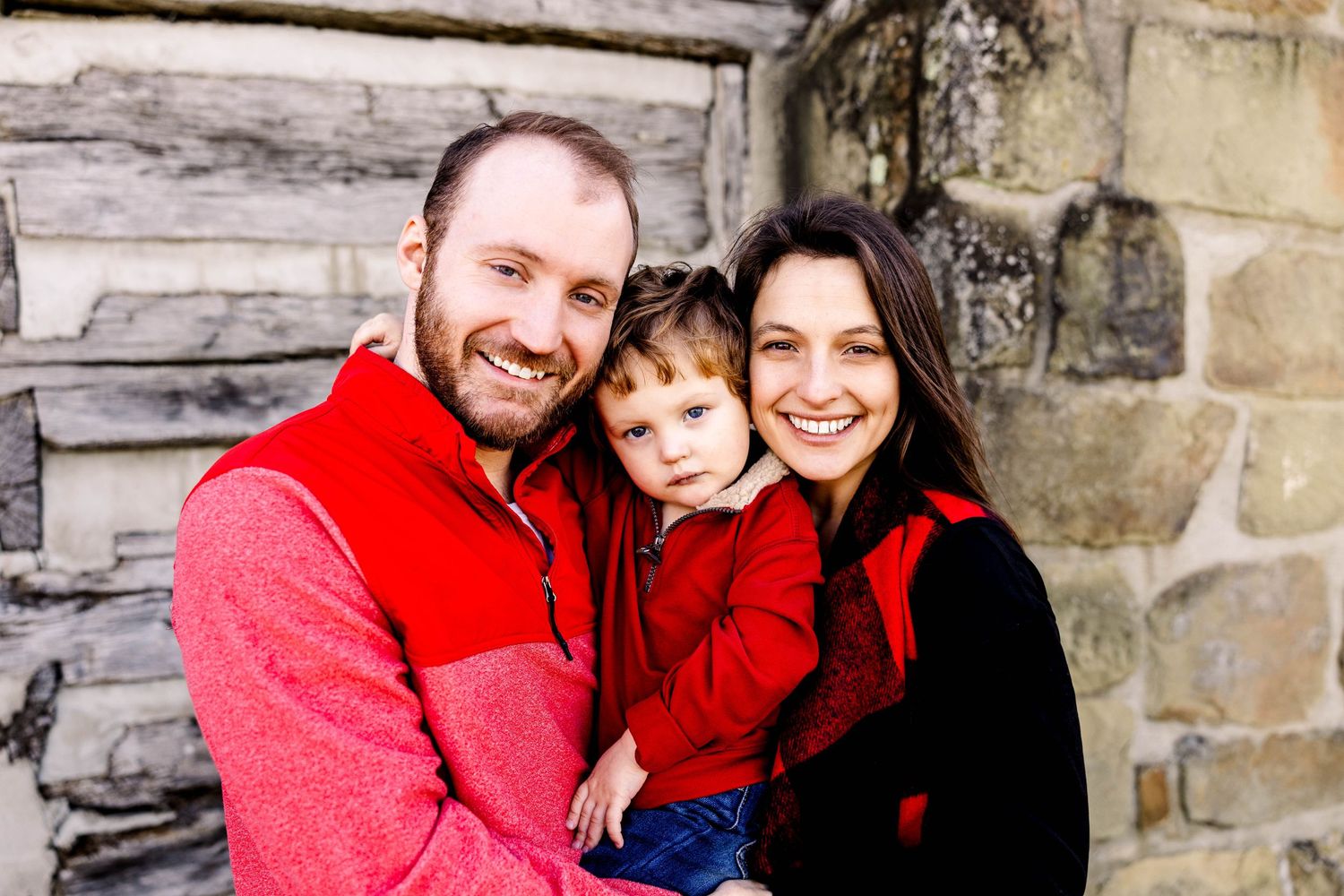 Family wearing coordinating red outfits posed against stone wall background.