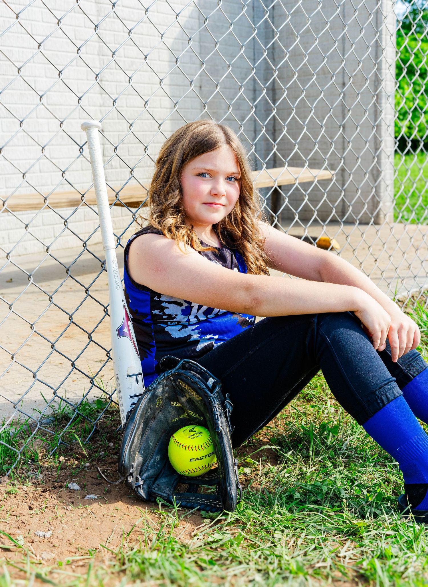 Softball player resting against fence with bat and glove.