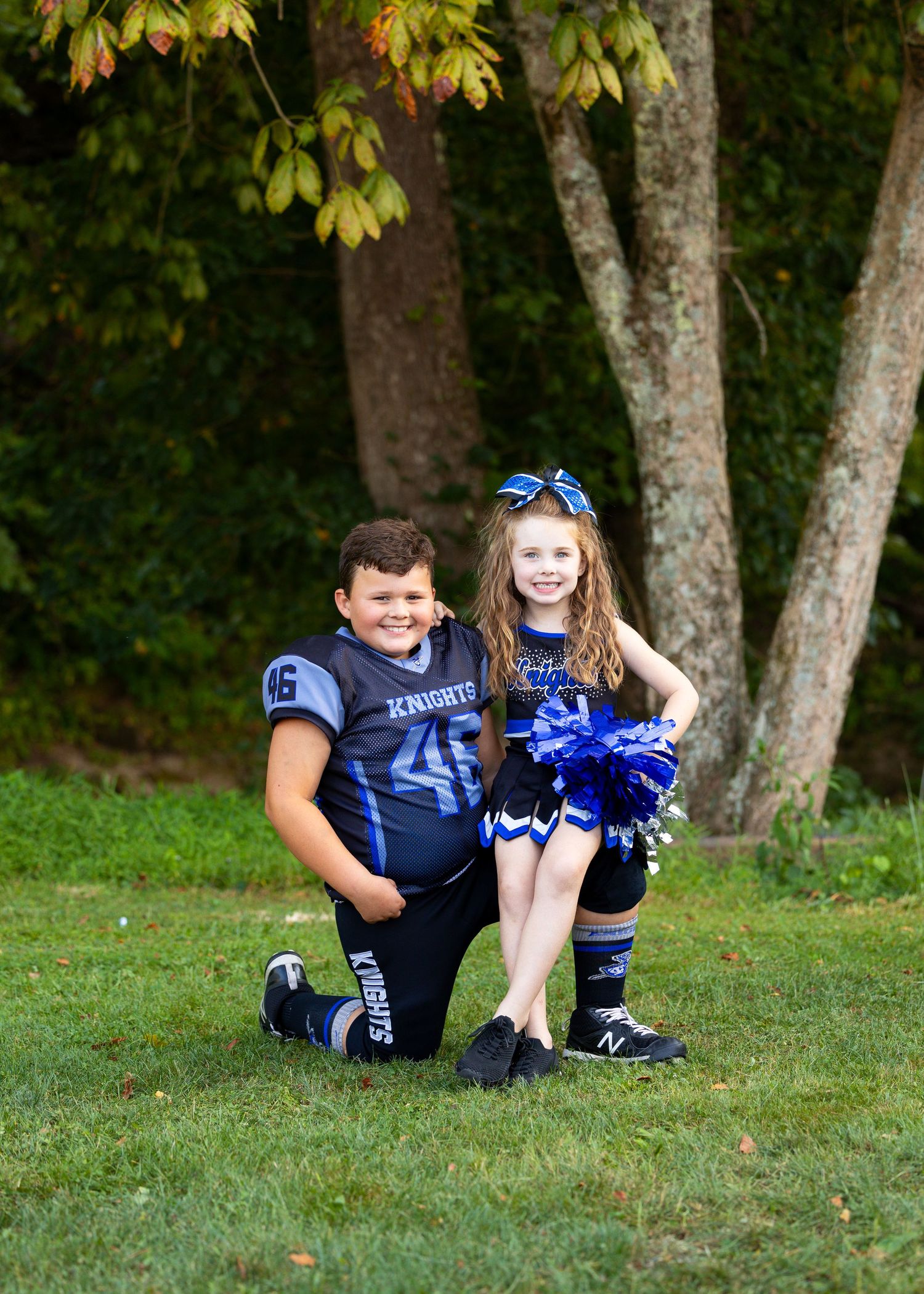 Football player and cheerleader in blue Knights uniforms pose together on grass.