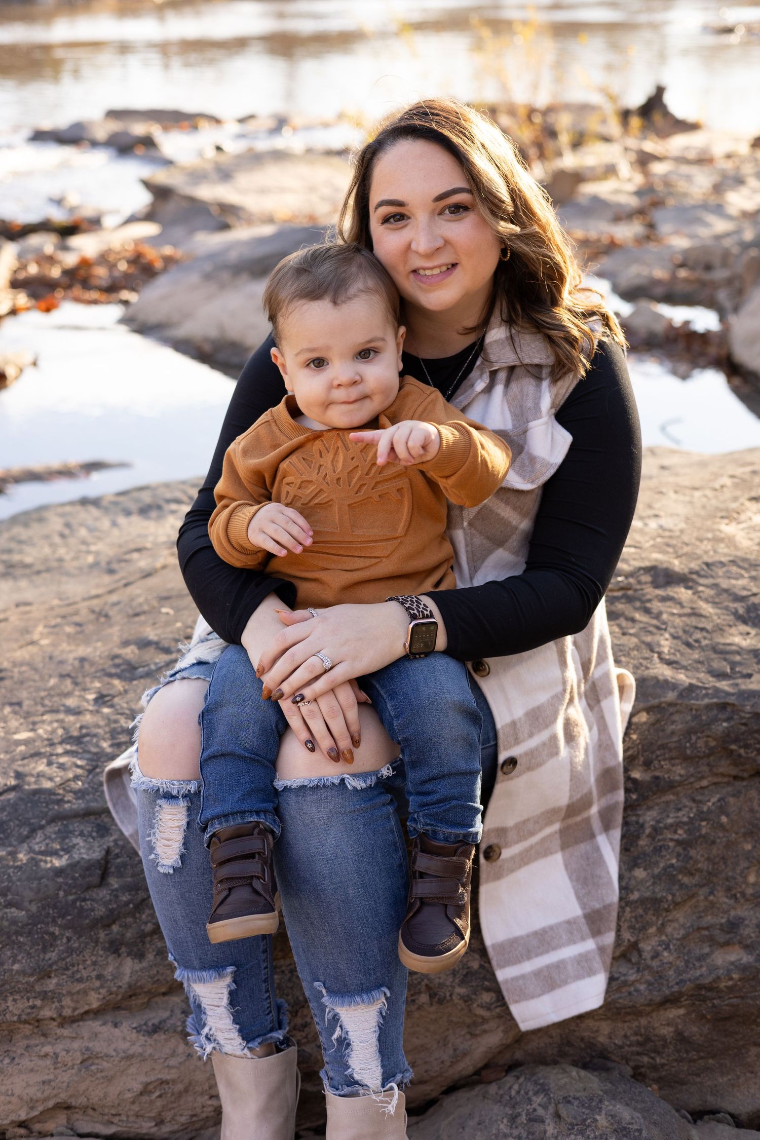 Parent and toddler in casual outfits sitting on rocks outdoors during a sunny day.