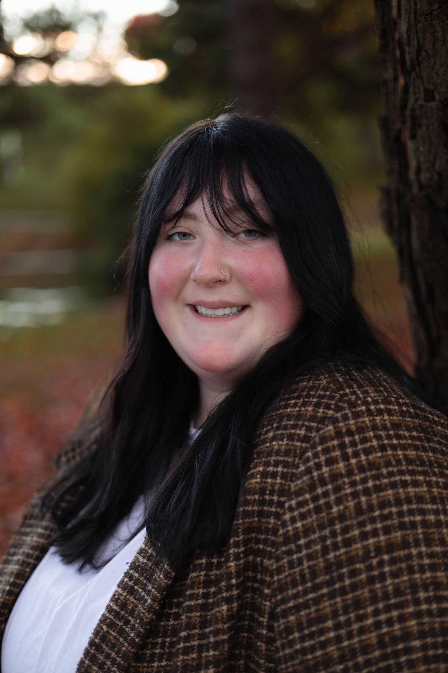 Portrait of person in brown tweed coat smiling outdoors in autumn.