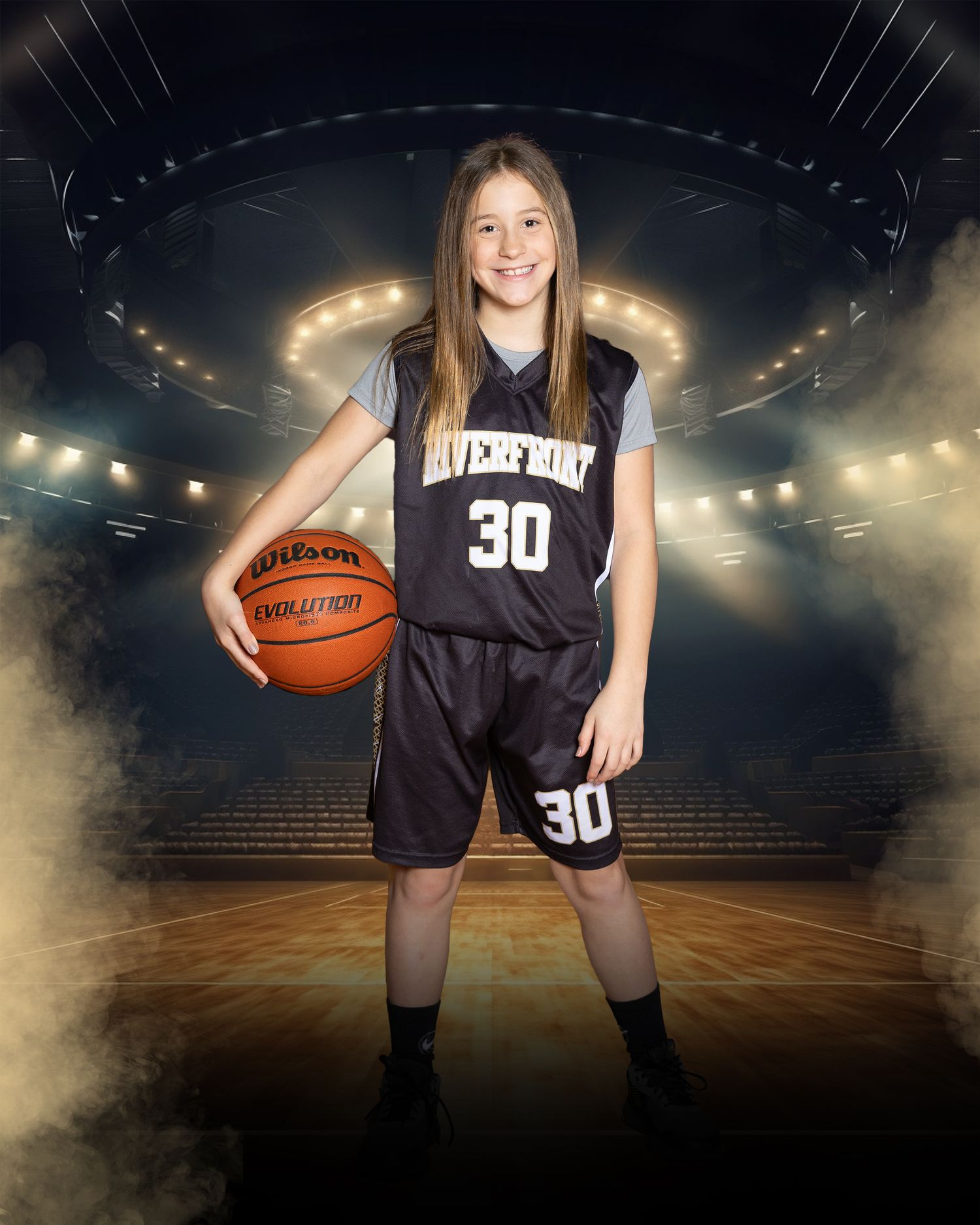 Youth basketball player in dark uniform holds ball on dramatically lit court.