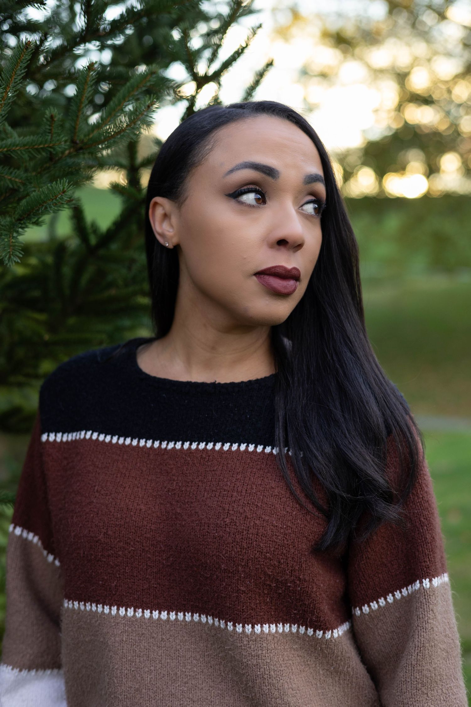 Portrait of woman in striped sweater looking to side against blurred natural background.