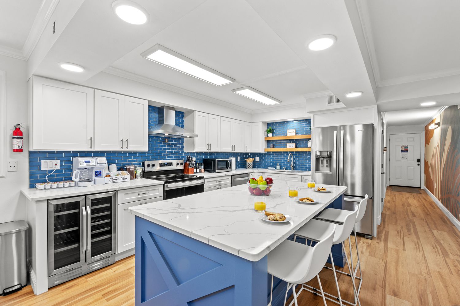 Modern kitchen with navy blue island, white cabinets, marble countertops and stainless steel appliances in bright space.