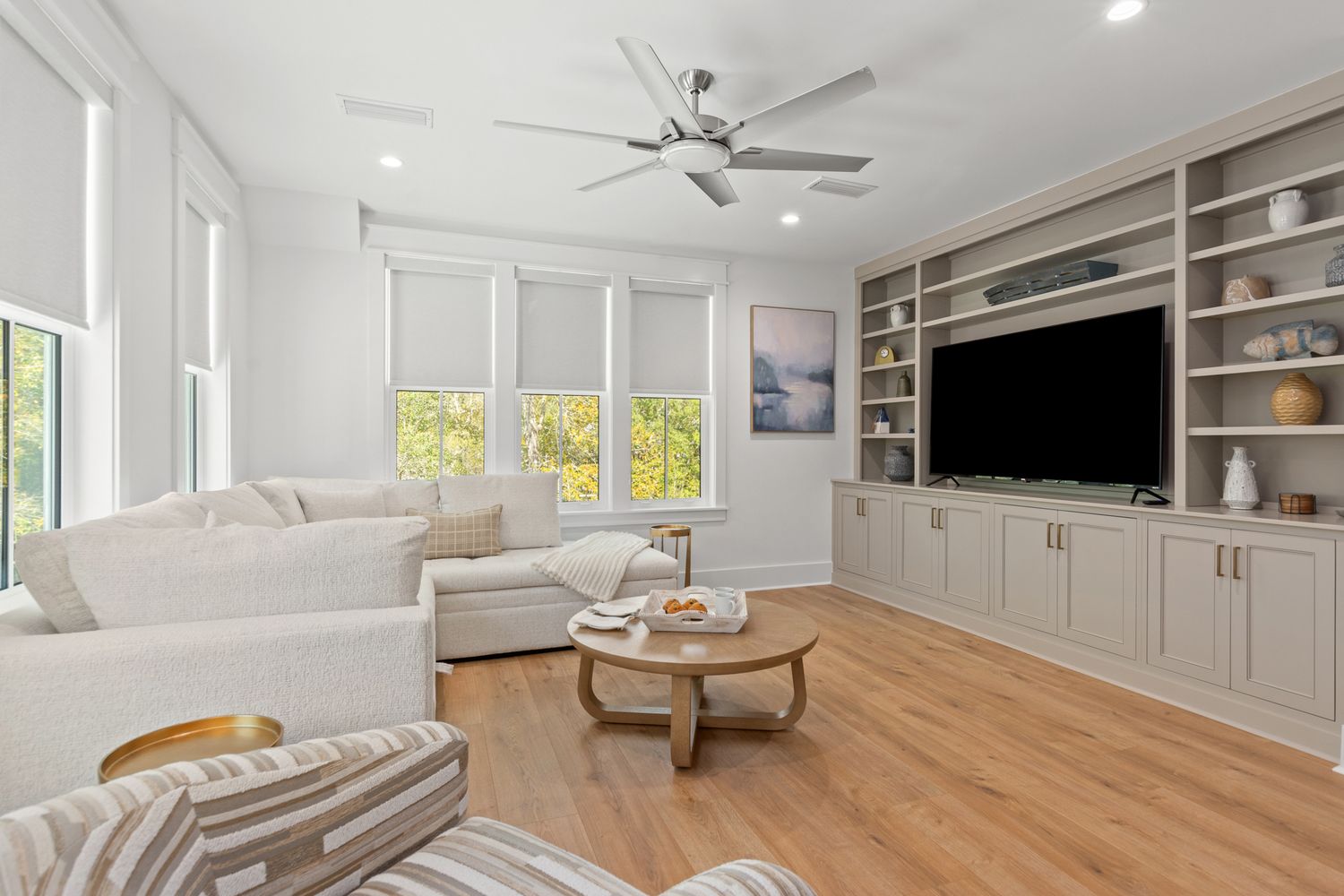 Modern coastal living room with built-in entertainment center, white slipcovered furniture, and hardwood floors.