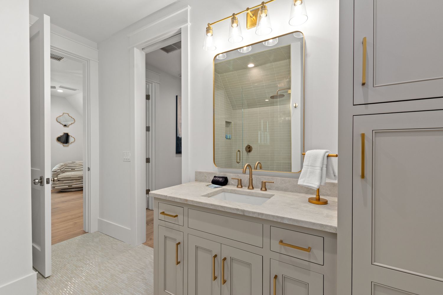 Gray bathroom vanity with gold hardware, framed mirror, and white walls features contemporary lighting fixtures.