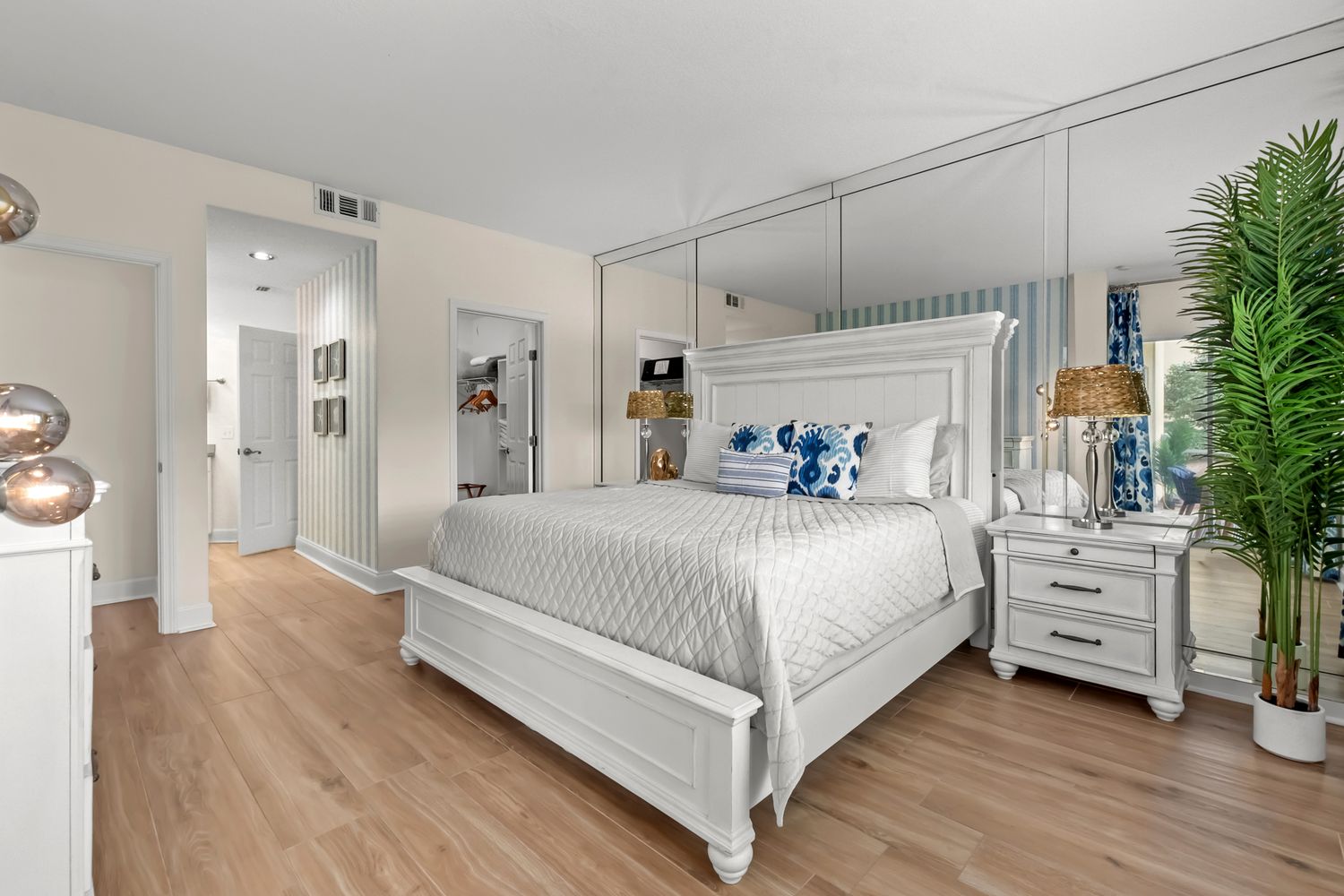 Modern white bedroom with mirrored accents, hardwood floors, potted plants, and natural lighting.