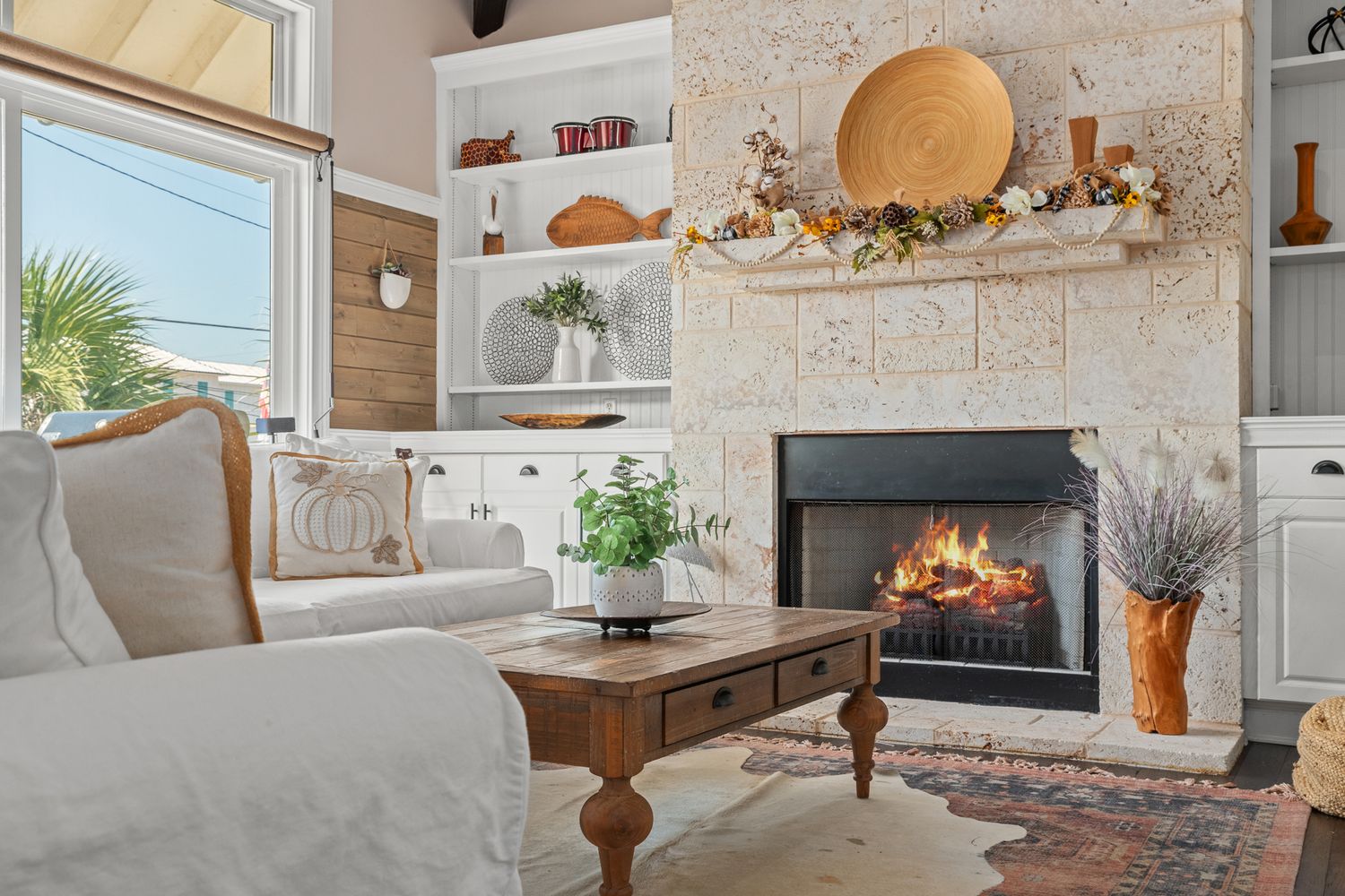 Cozy coastal living room with white built-ins, stone fireplace, and natural decor elements including woven baskets and plants.