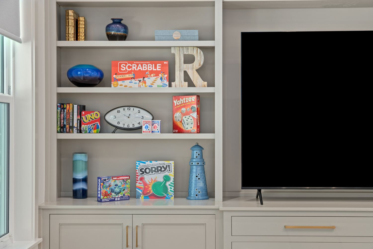 Built-in white shelving unit displays colorful retro decor items and books alongside a mounted flat screen TV.