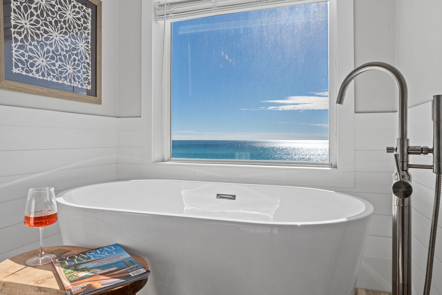 Large wall art and modern decor create a chic coastal living room with panoramic ocean views and plush white seating.