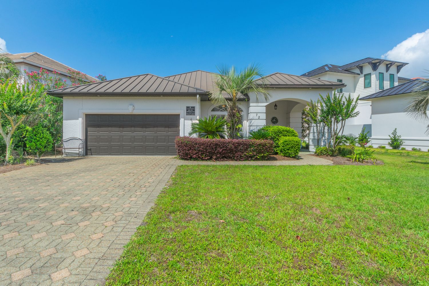 Single story Florida home with paver driveway, tropical landscaping and terra cotta tile roof against blue sky.