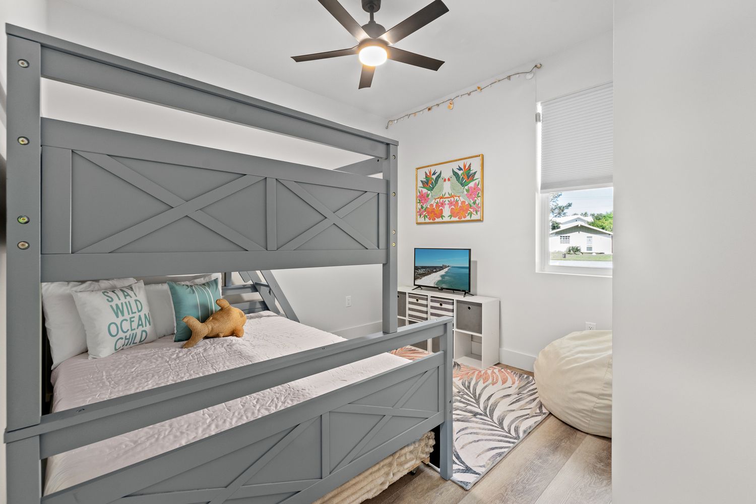 Modern bedroom featuring a gray farmhouse-style bed frame, coastal decor, and a ceiling fan in a bright white space.
