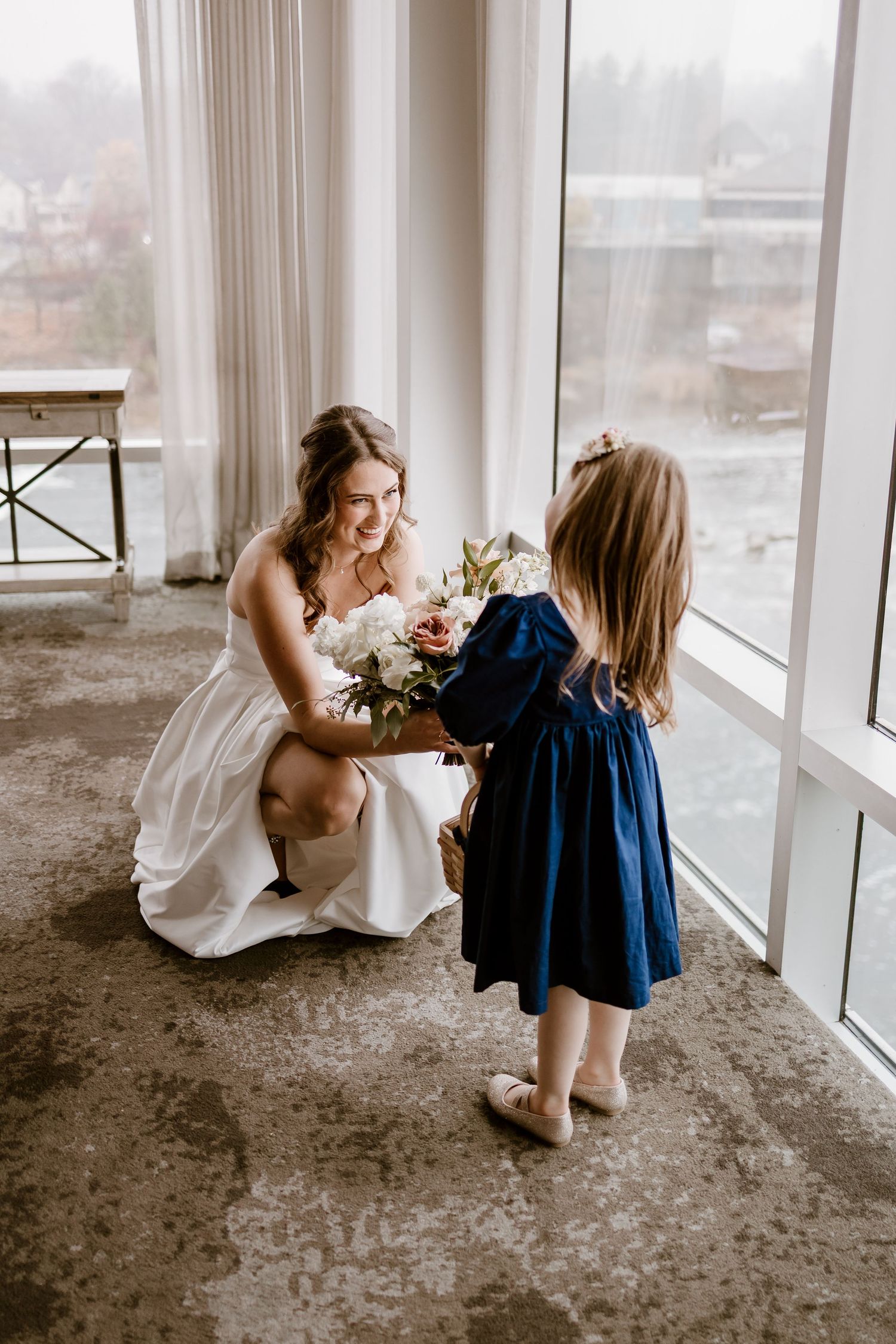 Candid wedding day preparations by a large window with white sheer curtains.