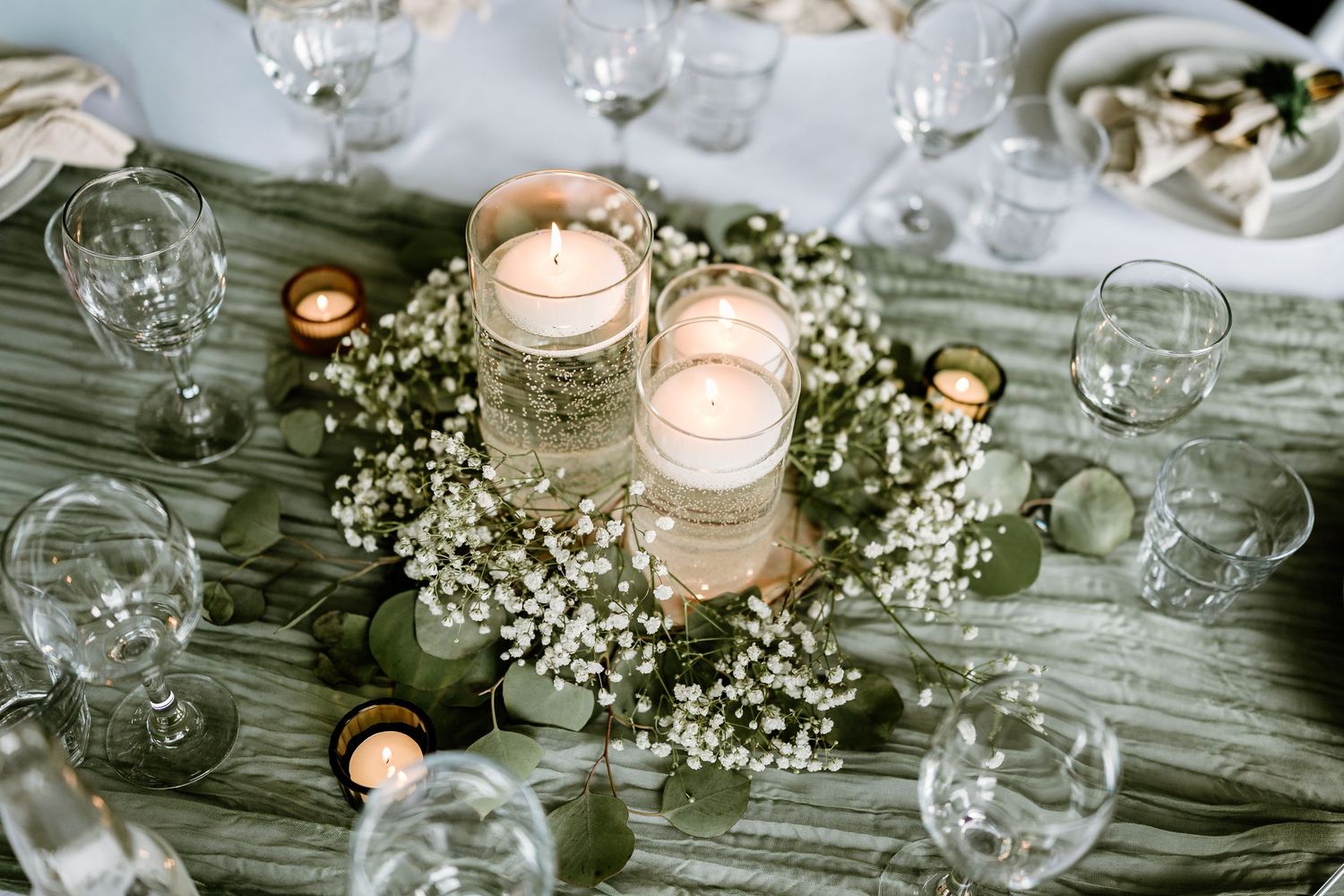 Rustic wedding table centerpiece with candles and baby's breath on wooden surface.