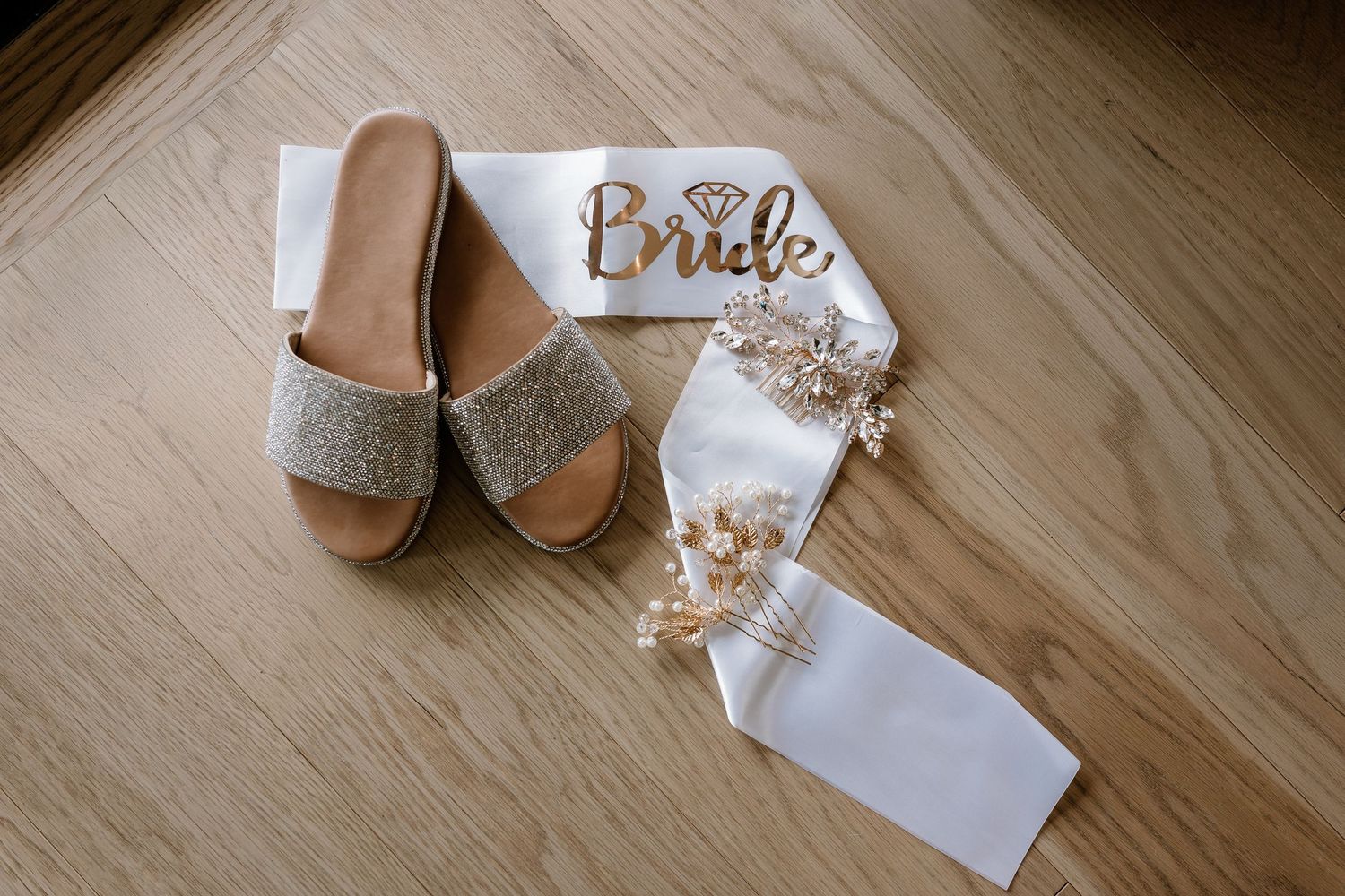 Wedding accessories including shoes and jewelry arranged on wooden floor.