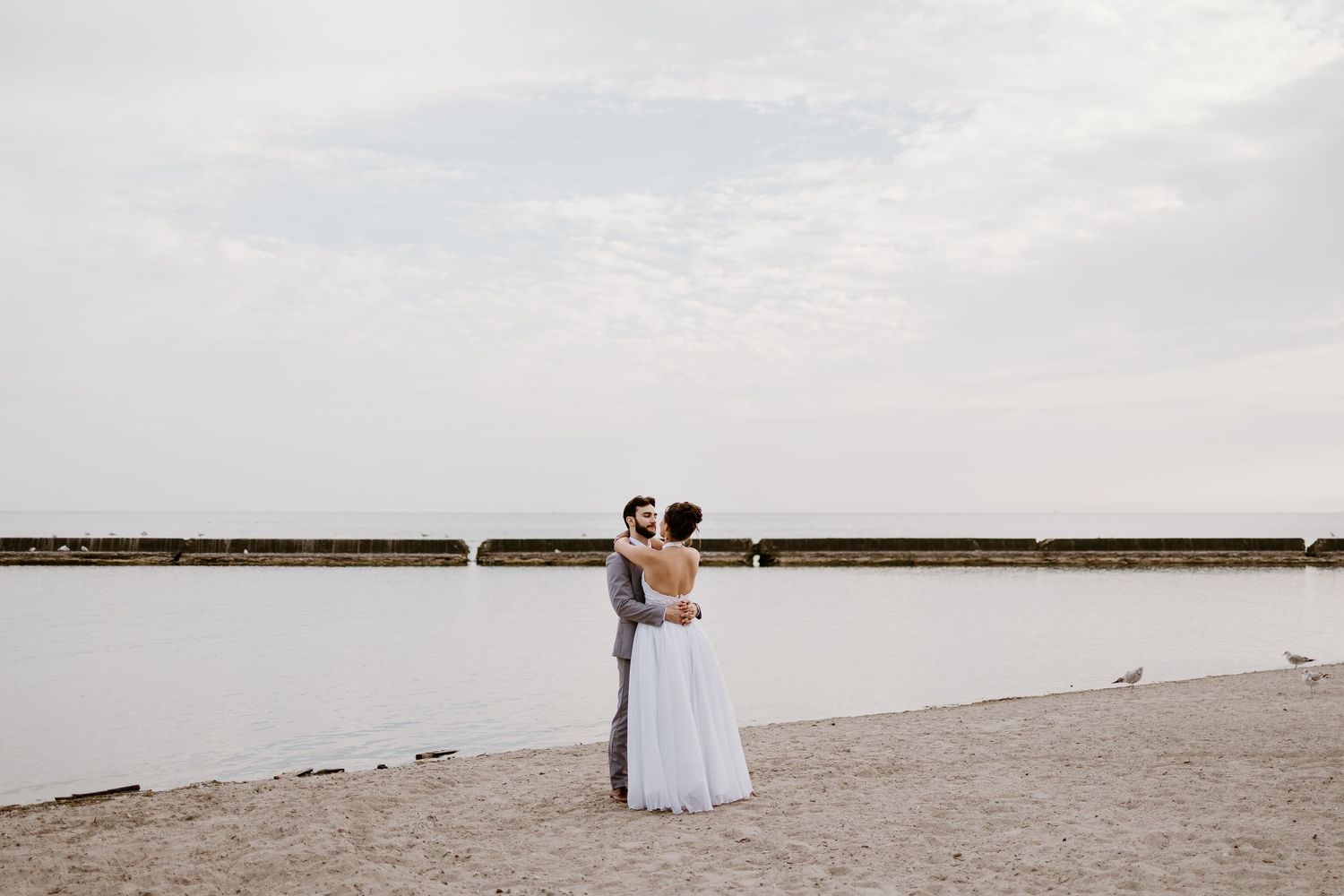 A wedding couple stands together on a beach pier during sunset.