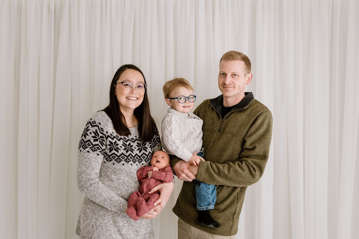 Family portrait against white curtain backdrop in coordinated neutral outfits.