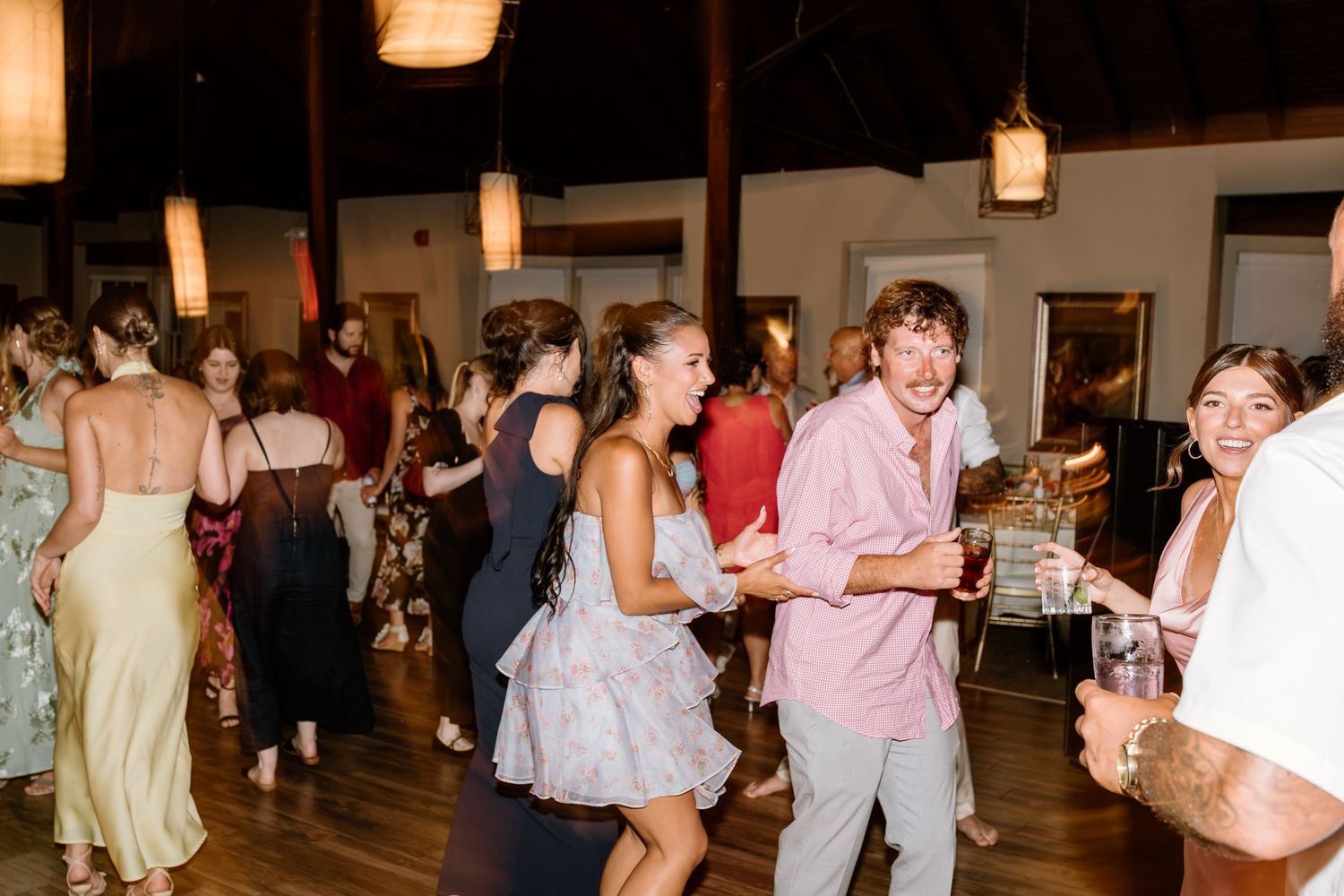 Guests dancing joyfully at an indoor wedding reception with warm pendant lighting and elegant decor.