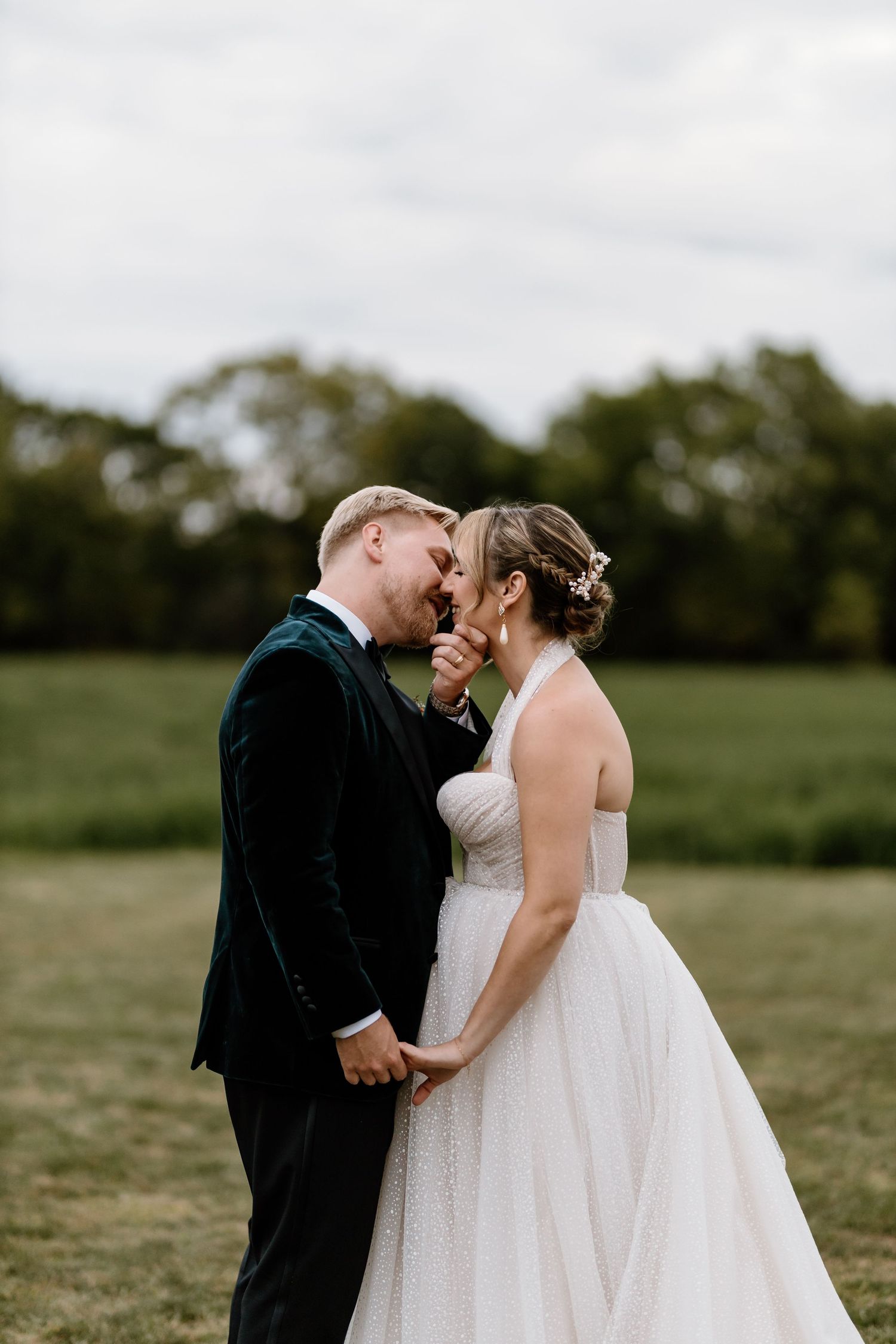 A couple shares an intimate moment in their wedding attire on a grassy field.
