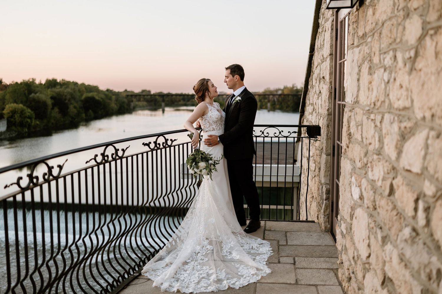 Wedding couple shares intimate moments along waterfront stone terrace at dusk.