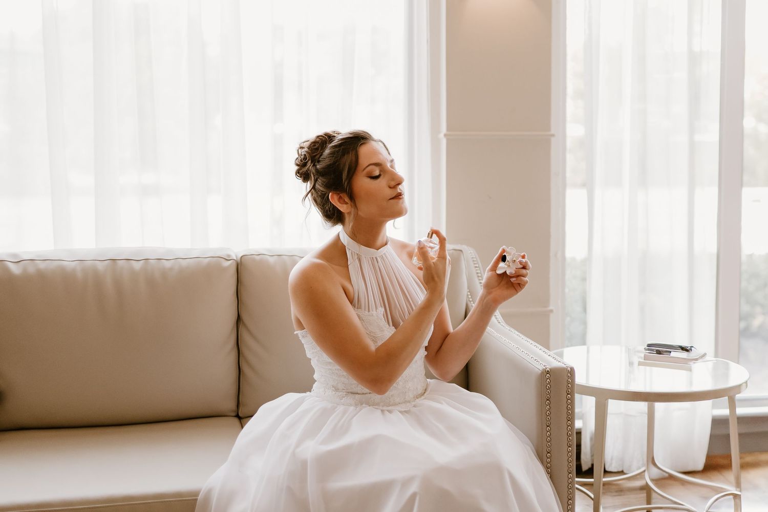 A person in a halter-neck white wedding dress sits elegantly on a cream sofa.