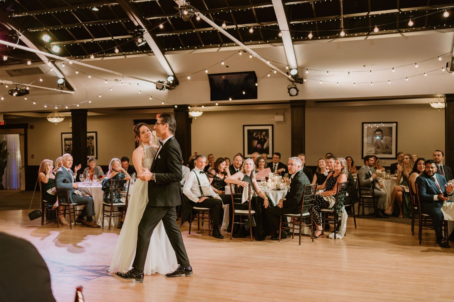 Wedding reception dance floor surrounded by seated guests in an elegantly lit venue.