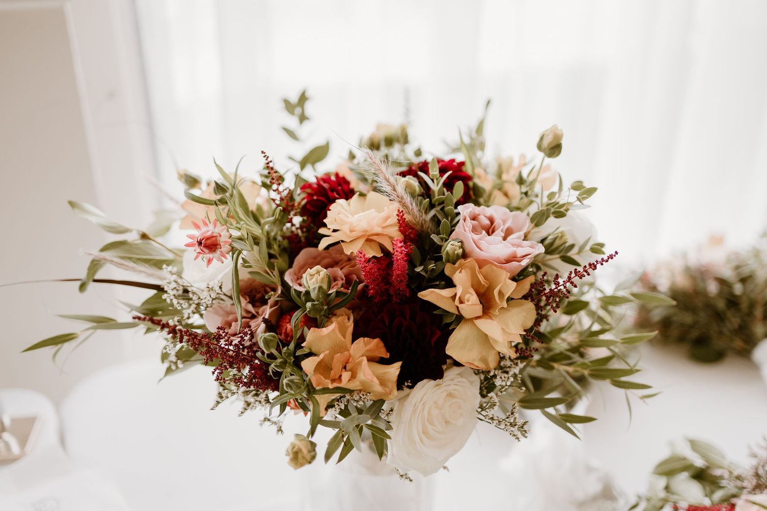 Elegant floral arrangement featuring peach and pink blooms with greenery on a white background.