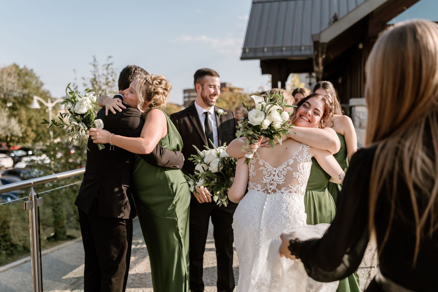 Wedding party shares emotional embraces on an outdoor terrace with bridesmaids in green dresses.