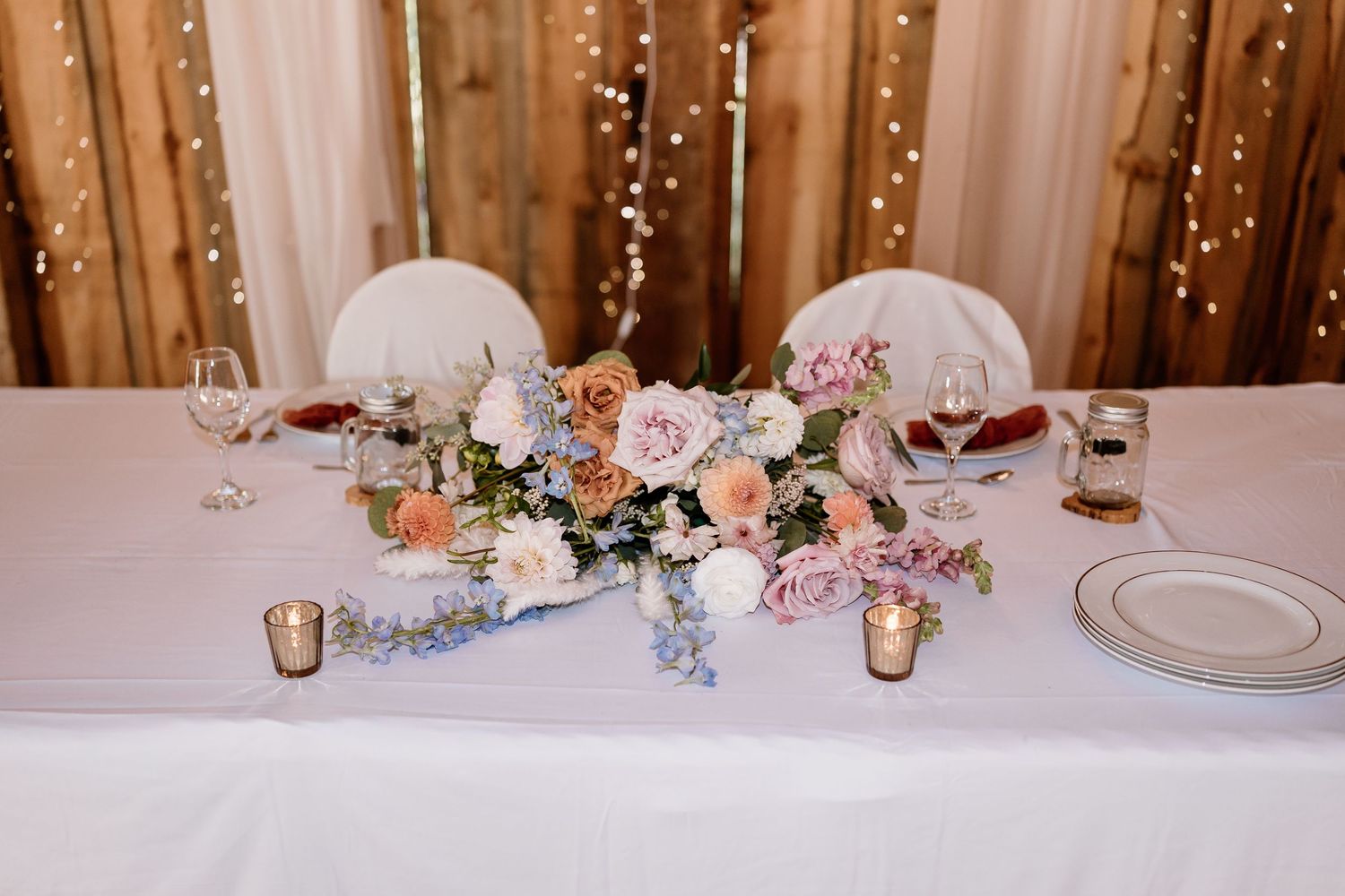 Elegant wedding reception table with soft lighting and floral centerpieces in rustic barn setting.