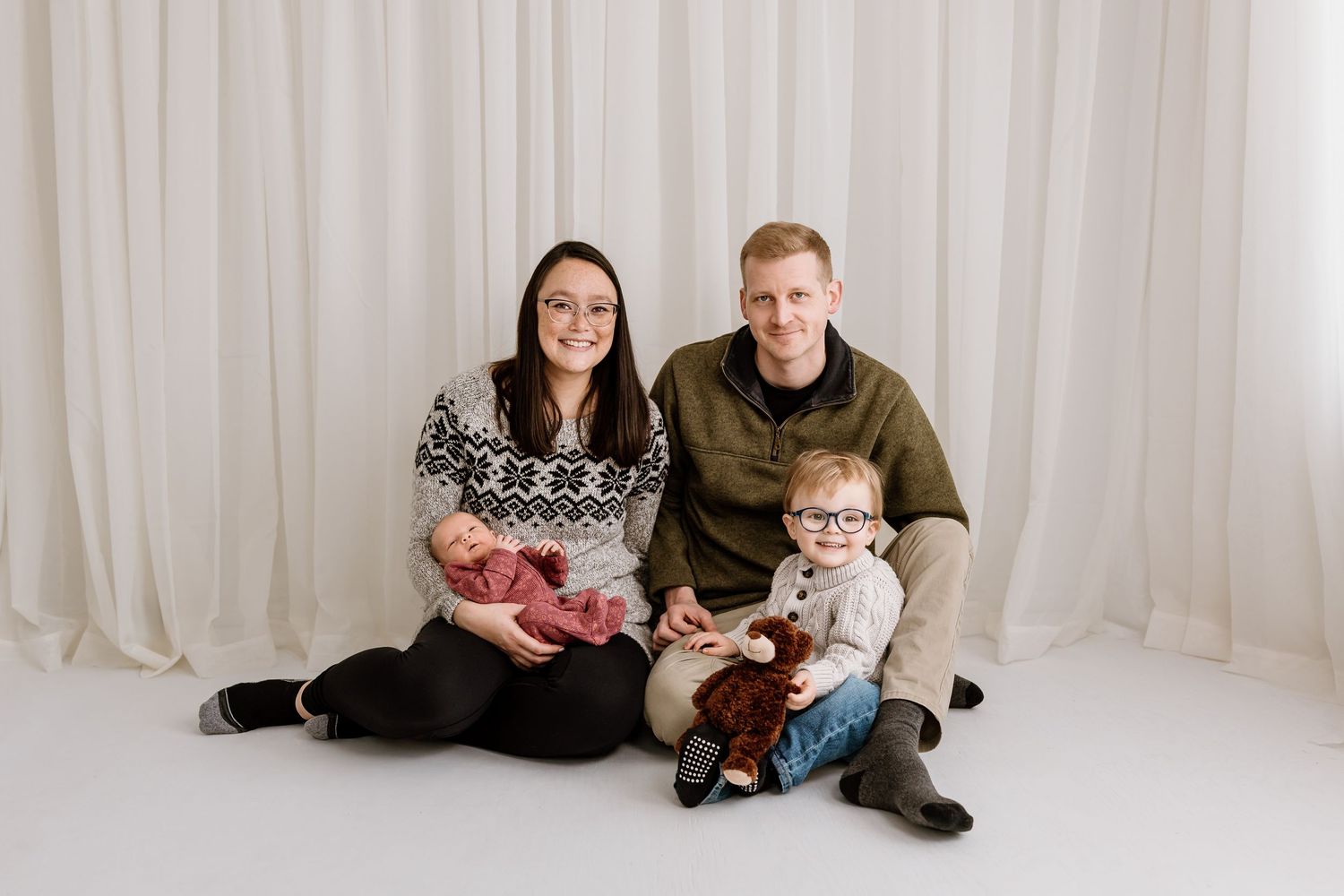 Family group poses together on floor during indoor studio photography session.