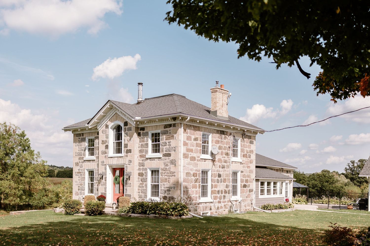 Stone farmhouse exterior with wraparound porch on a sunny day with blue skies.
