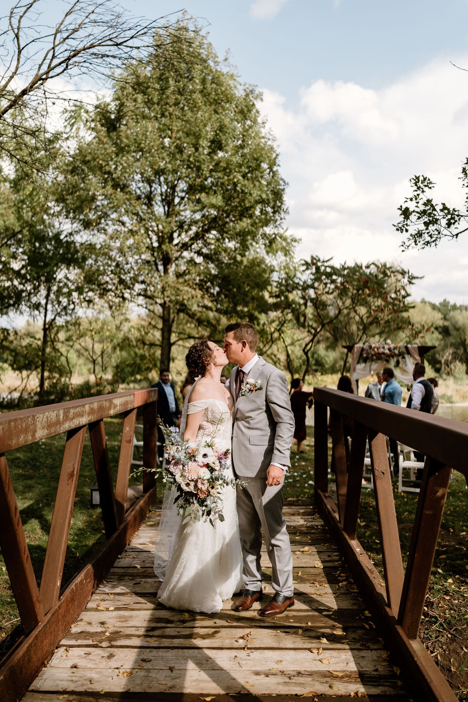 Wedding couple shares a romantic moment on a wooden bridge surrounded by autumn trees.