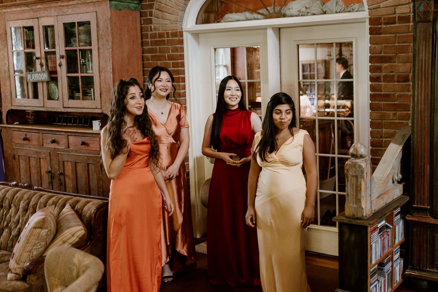 Bridesmaids in colorful silk dresses pose together in an elegant room with arched doorways.
