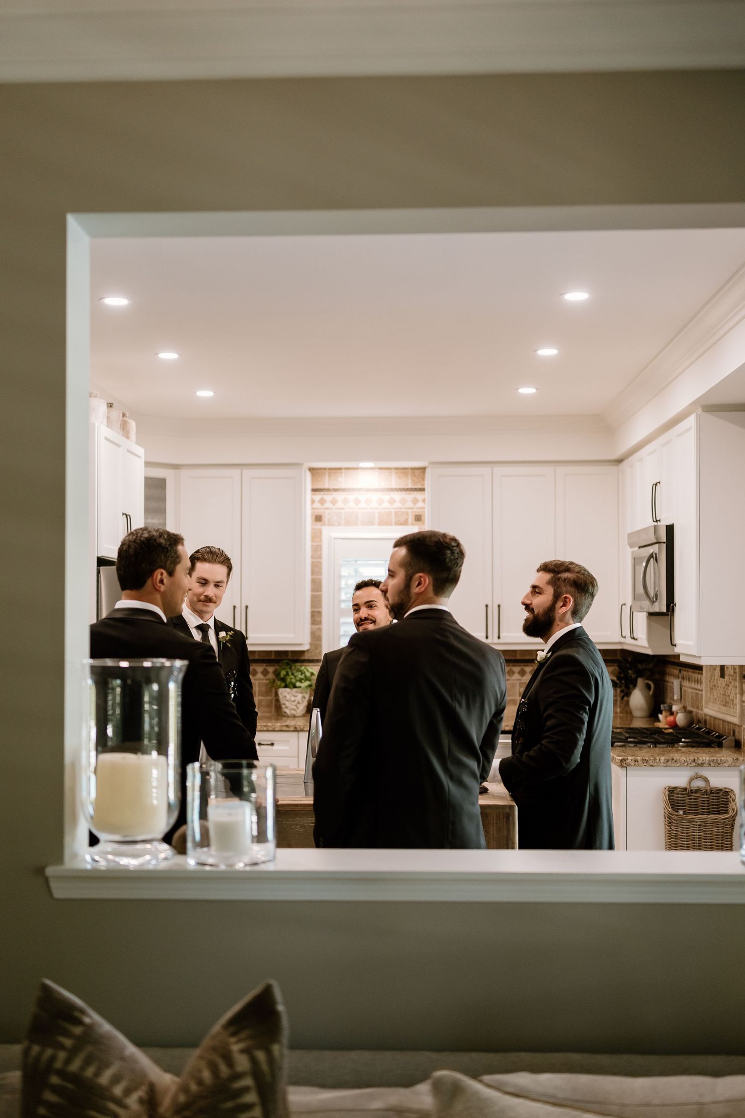 Groomsmen gather in a modern white kitchen space during wedding preparations.