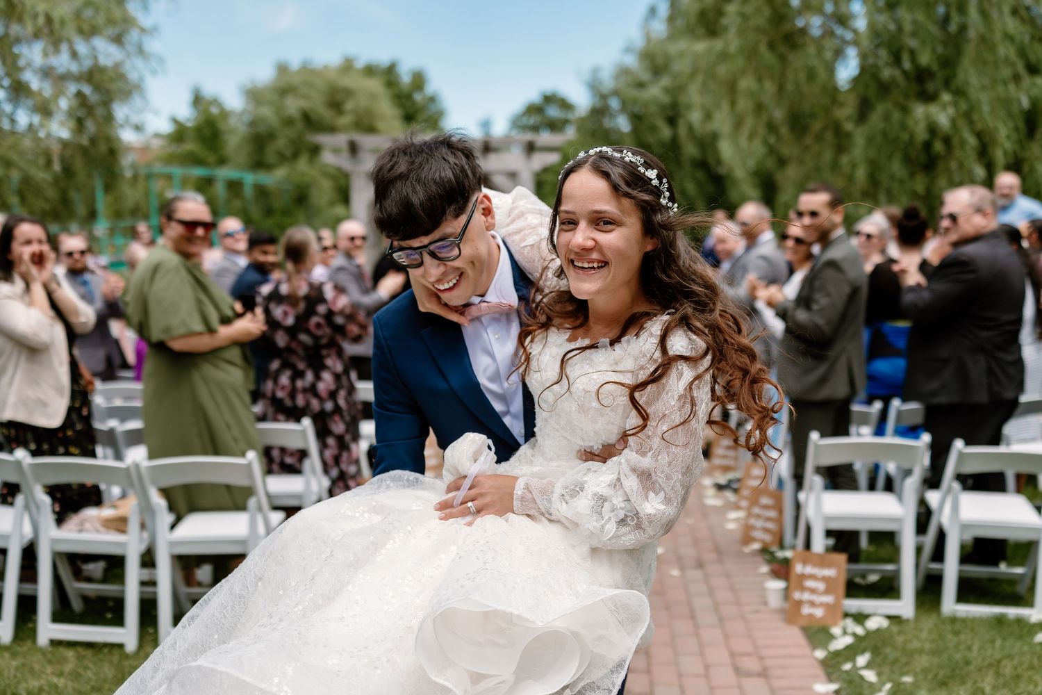 Two brides celebrate joyfully after their outdoor wedding ceremony, surrounded by cheering guests on a sunny day.