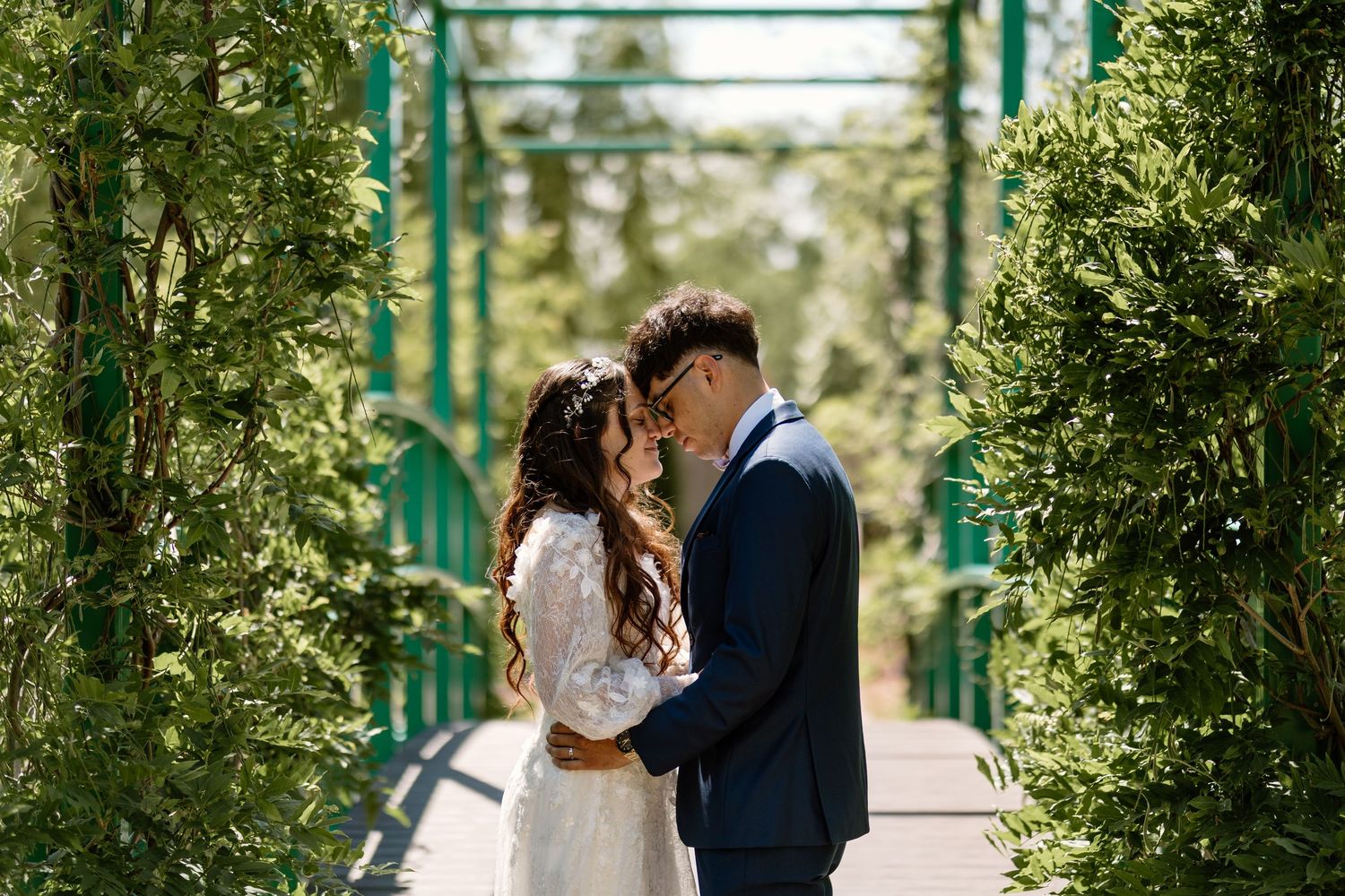 Bride and groom share a romantic moment on a green bridge surrounded by lush foliage on their wedding day.
