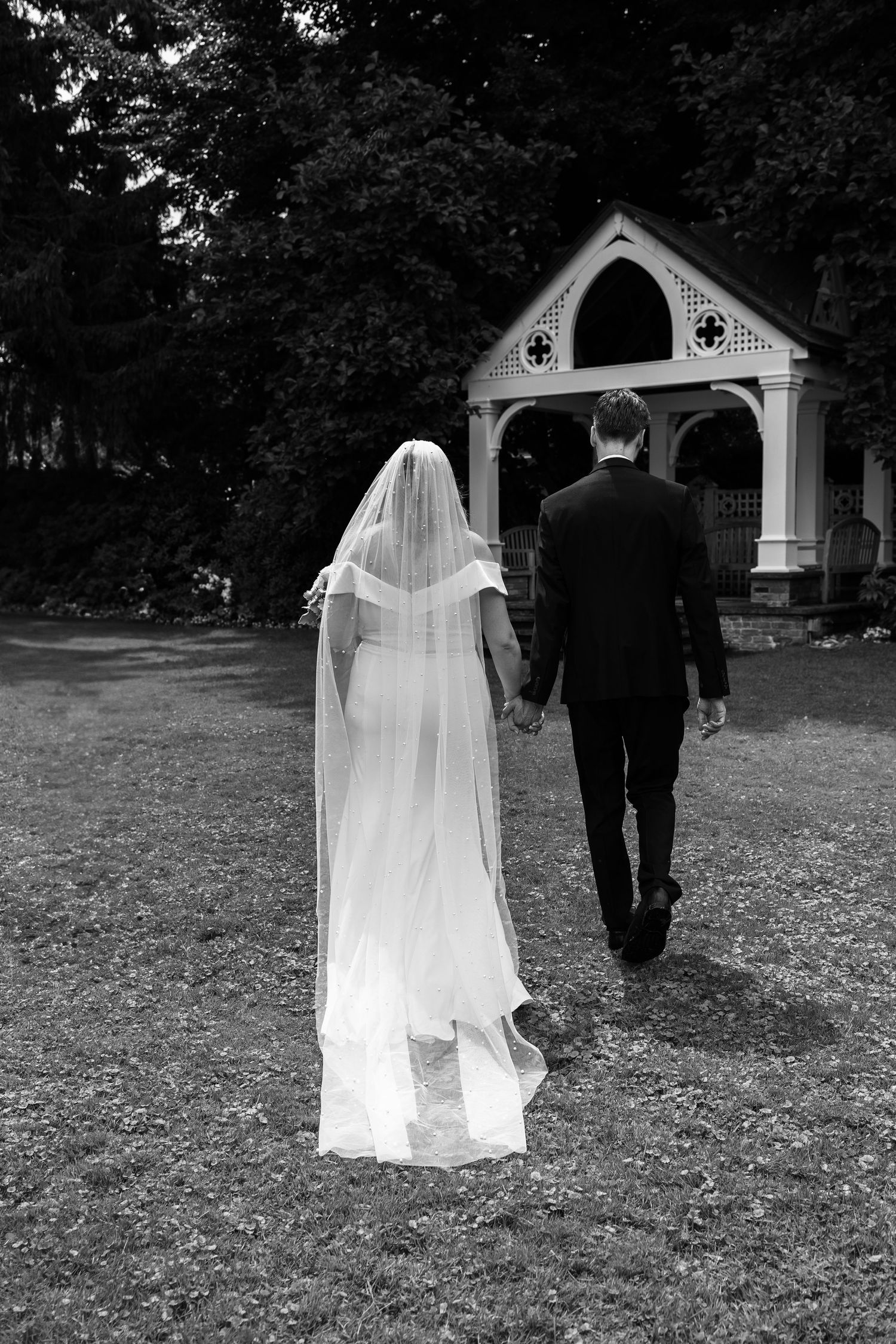 Wedding couple walking through fallen leaves toward a chapel in black and white photography.
