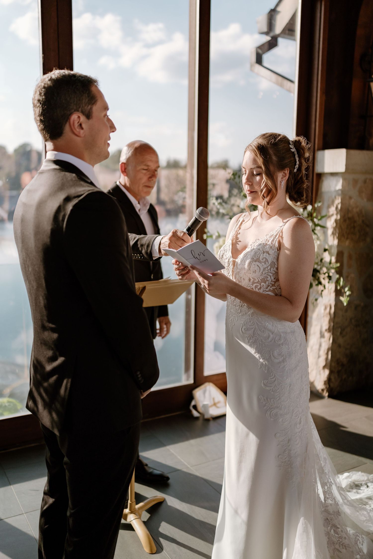 Intimate wedding ceremony with couple reading vows in front of panoramic windows.