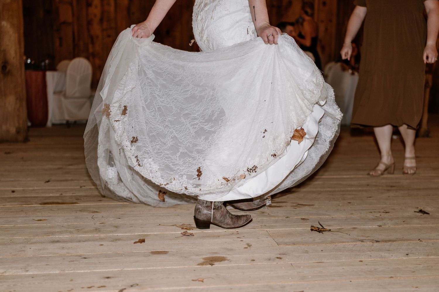 Close-up of white wedding dress hem swirling on rustic wooden floor during dance.